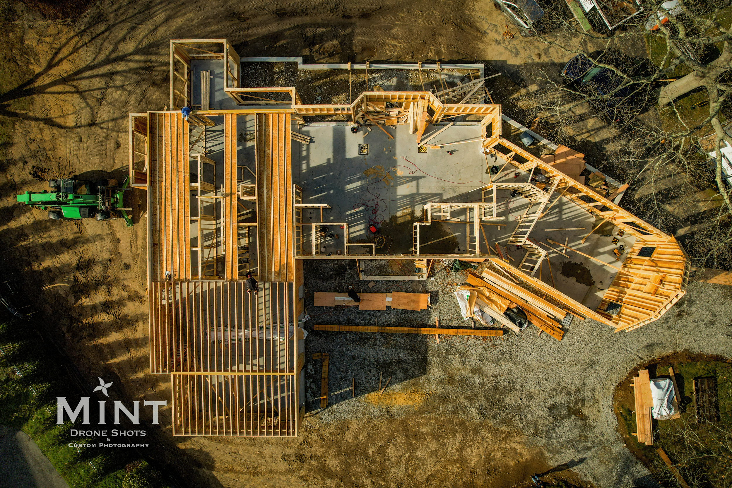 Aerial view of a house under construction with visible wooden framing and construction materials on the site.