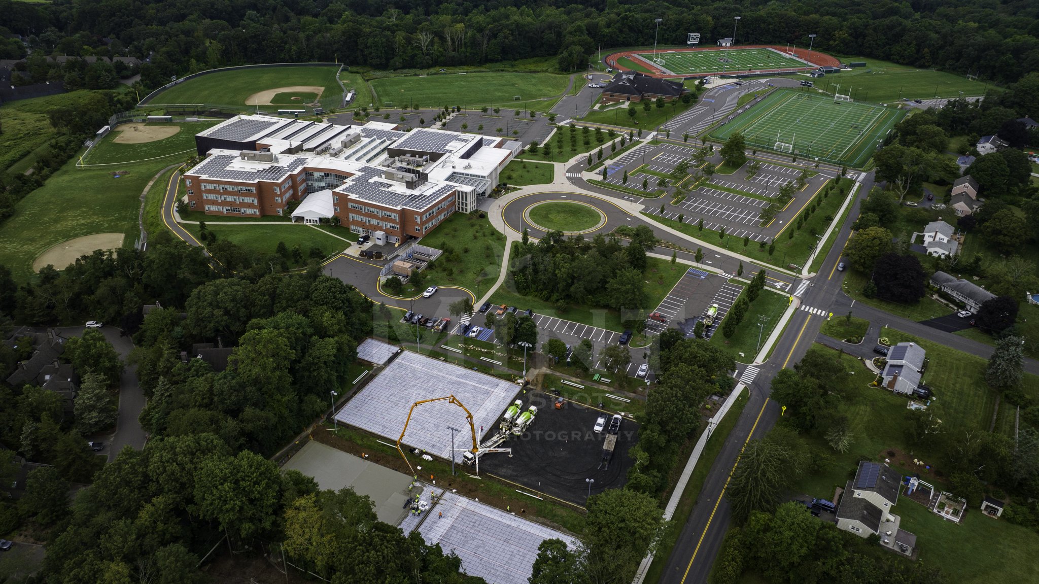 Aerial view of a school campus with sports fields, parking lots, and surrounding residential area.