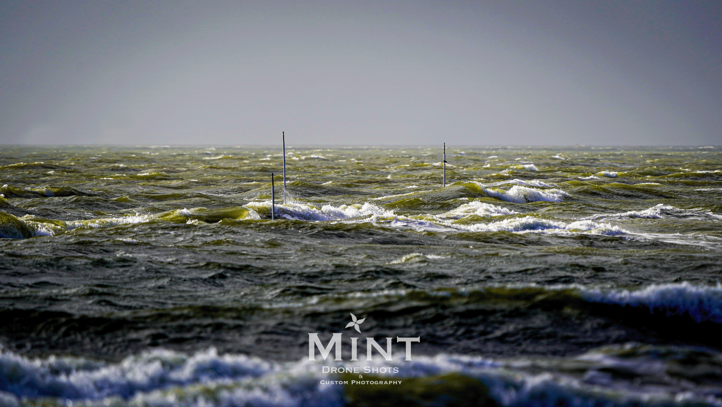 Choppy ocean waves with protruding poles and gray sky