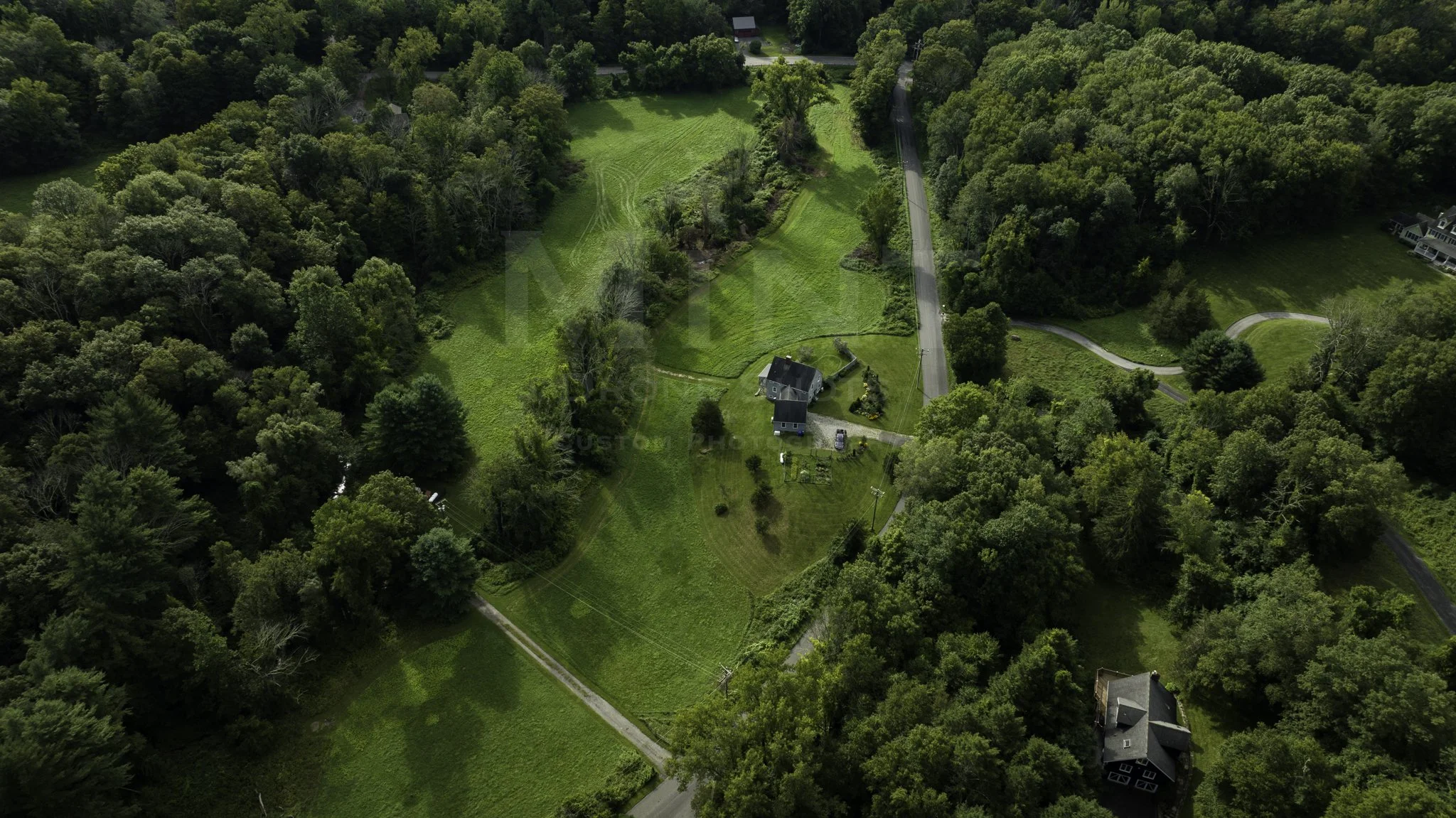 Aerial view of a rural landscape with a house surrounded by greenery and trees, intersected by roads.