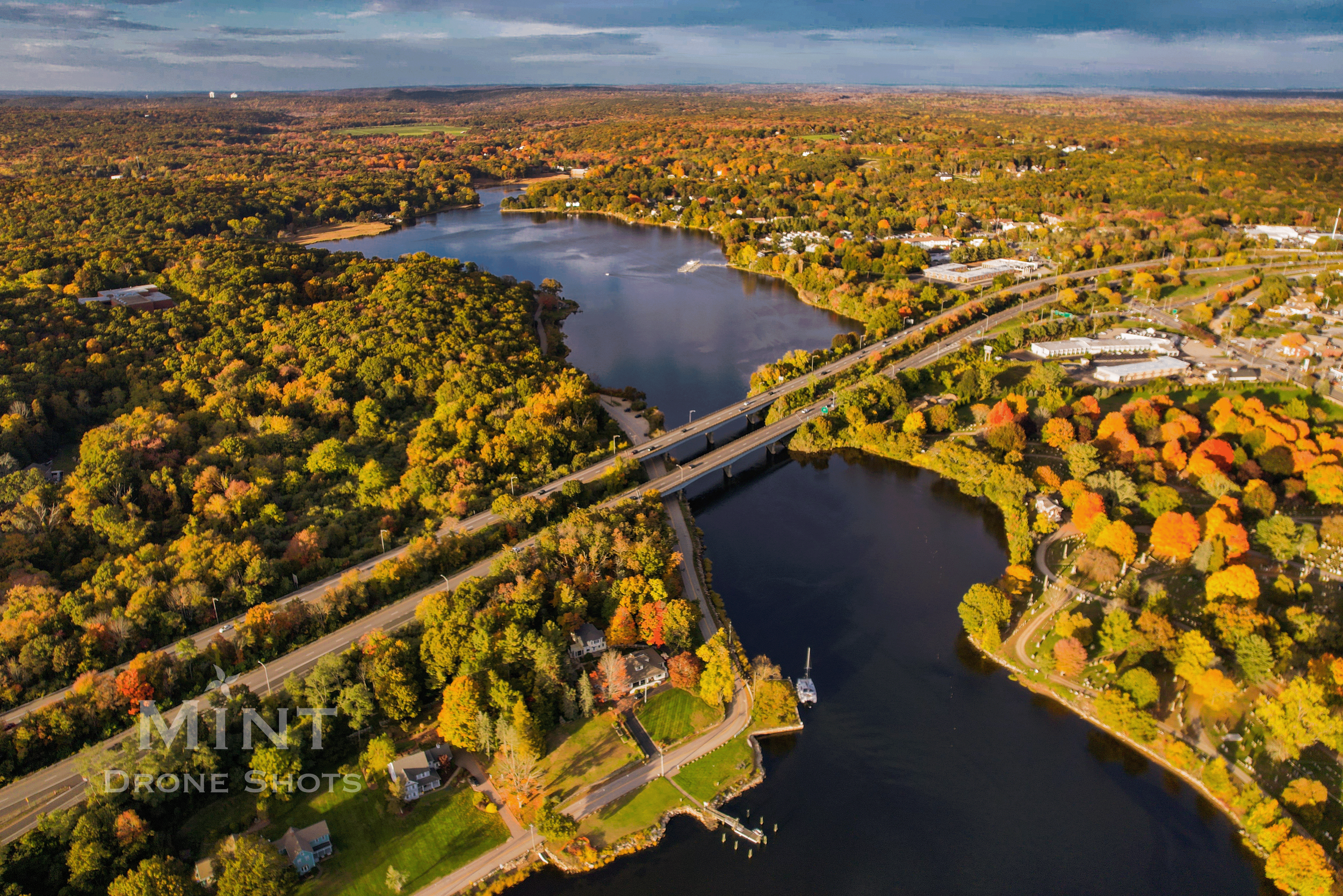 Aerial view of a river with a bridge, surrounded by autumn foliage and roads weaving through colorful trees.