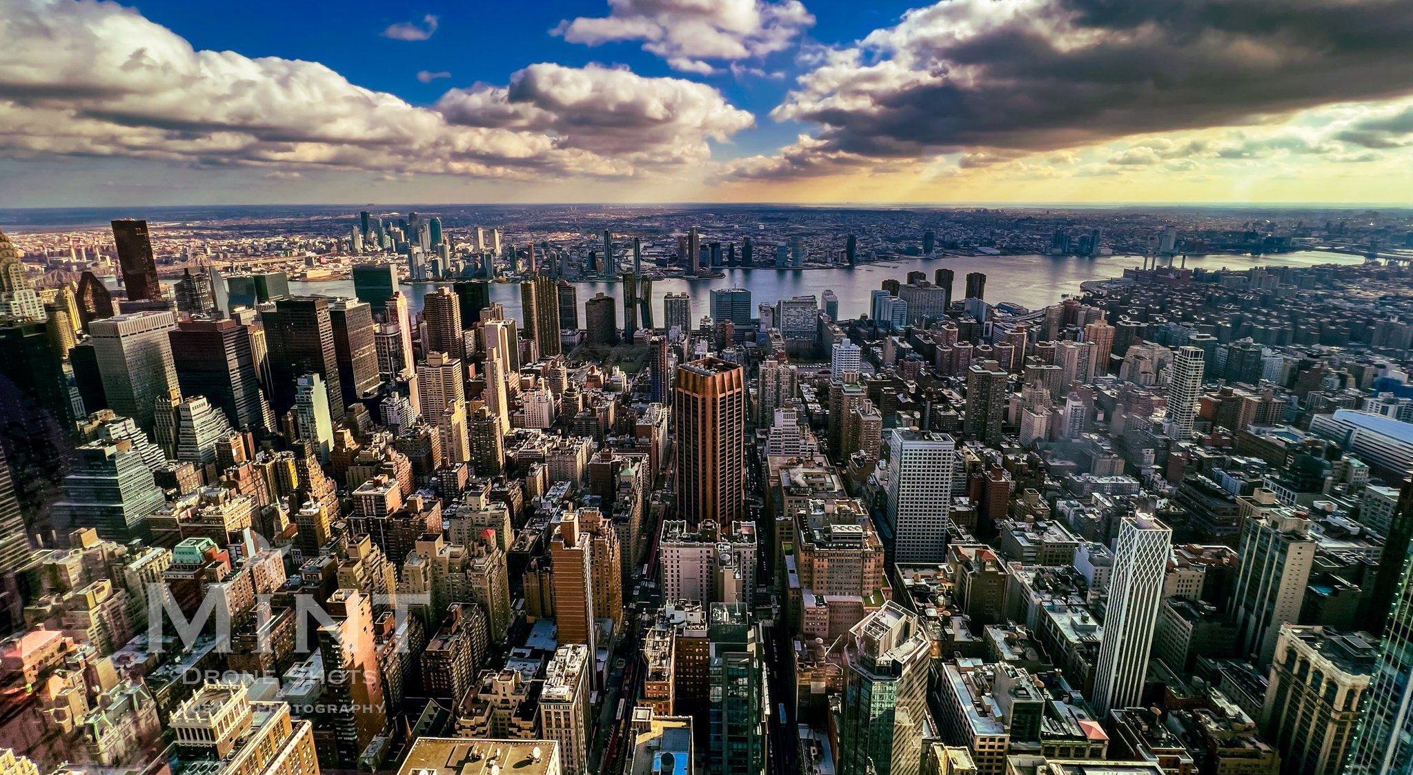 Aerial view of New York City skyline with skyscrapers and East River under a cloudy sky.