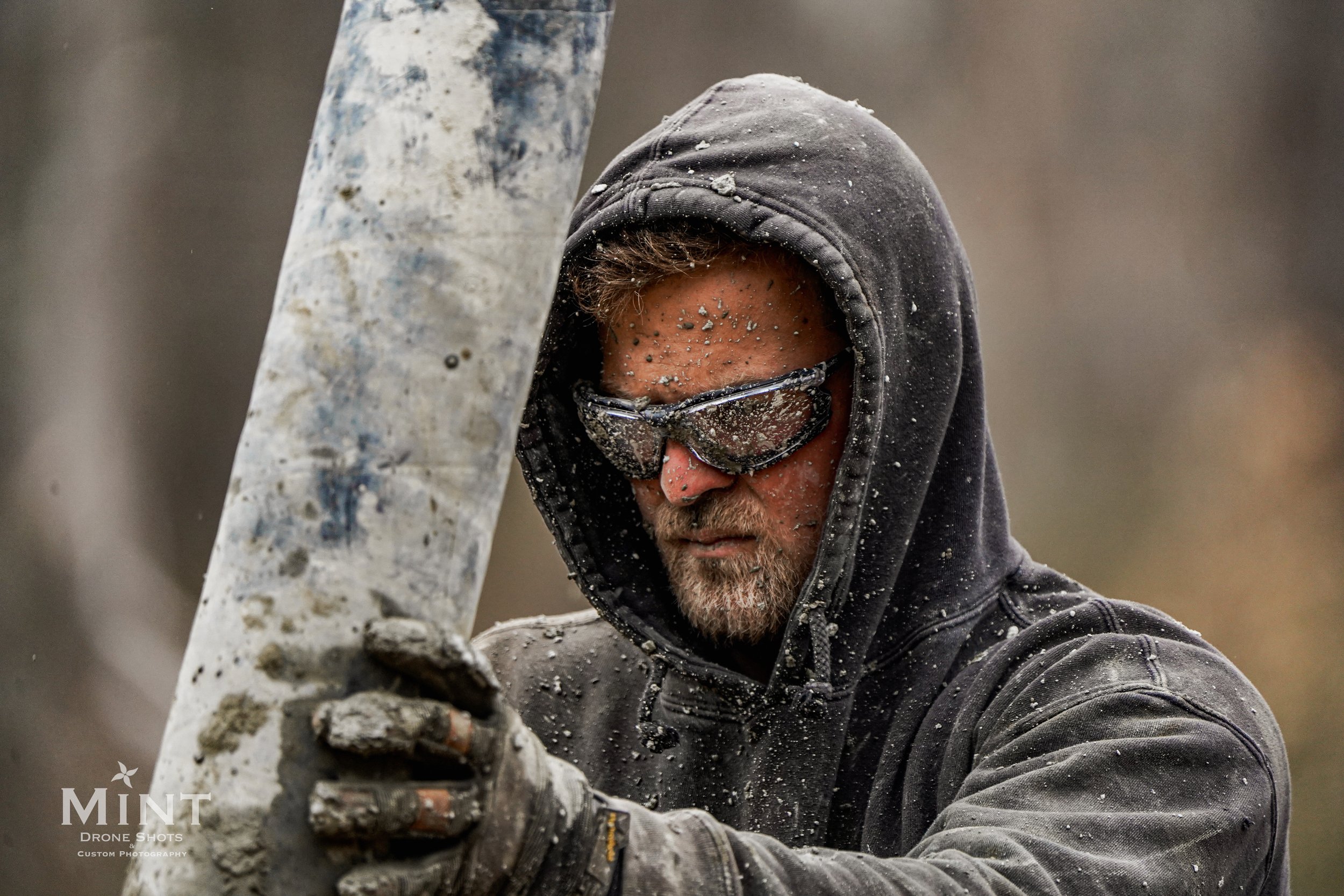 Man in a hoodie and safety goggles holding a large, dirty metal pole.