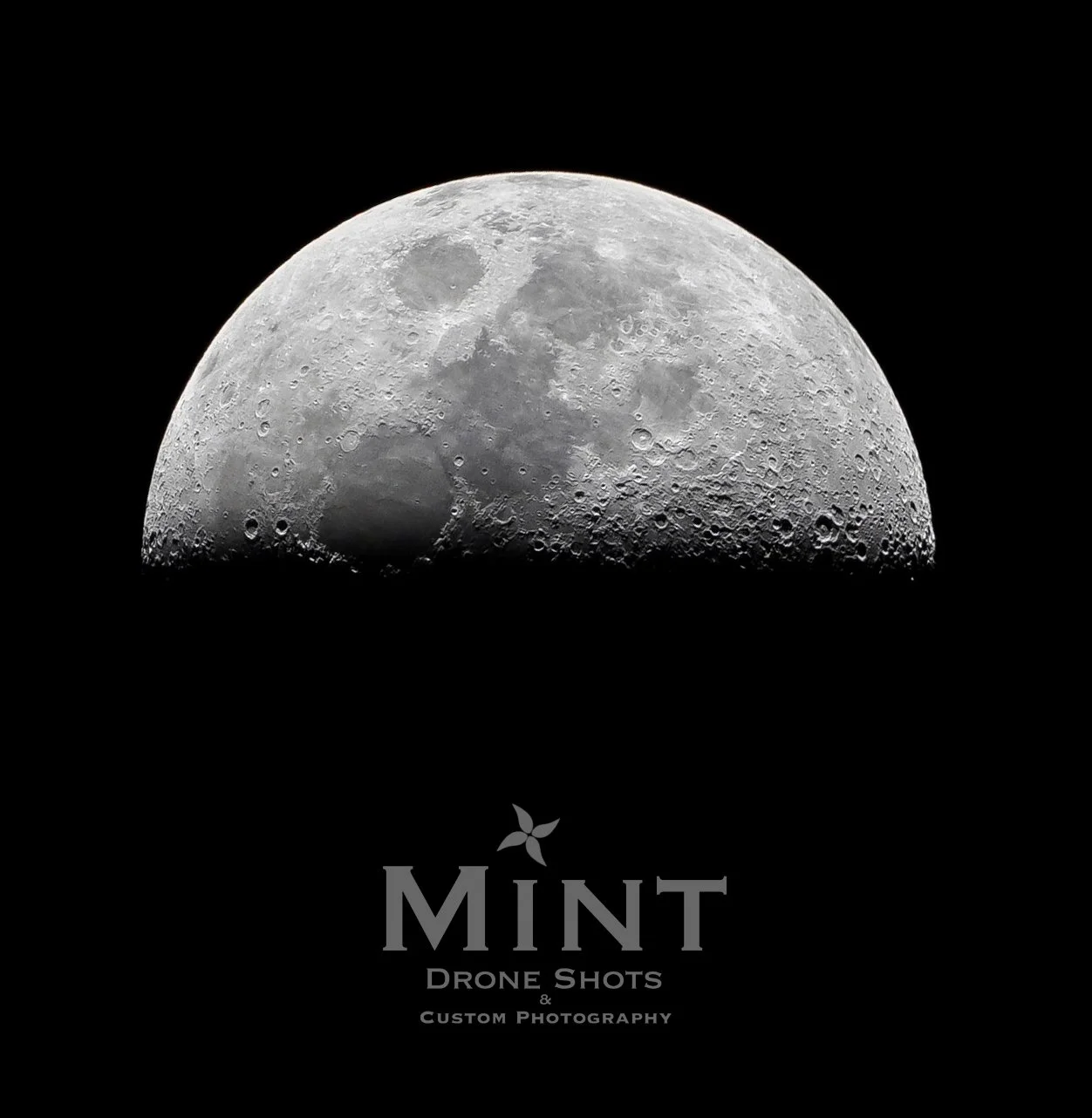 Half moon with visible craters and texture, photographed against a black background. "Mint Drone Shots & Custom Photography" text below the moon.