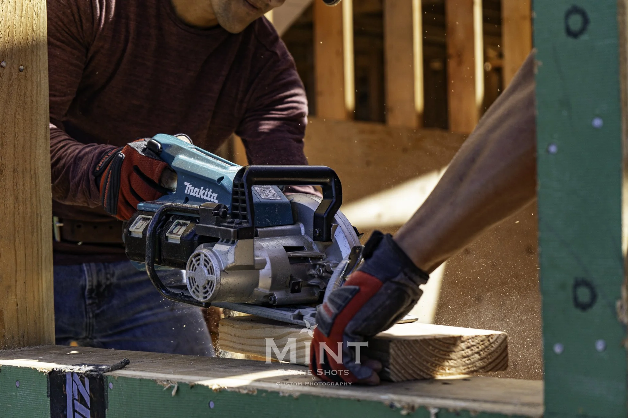 Two construction workers using a Makita circular saw to cut wood on a construction site.