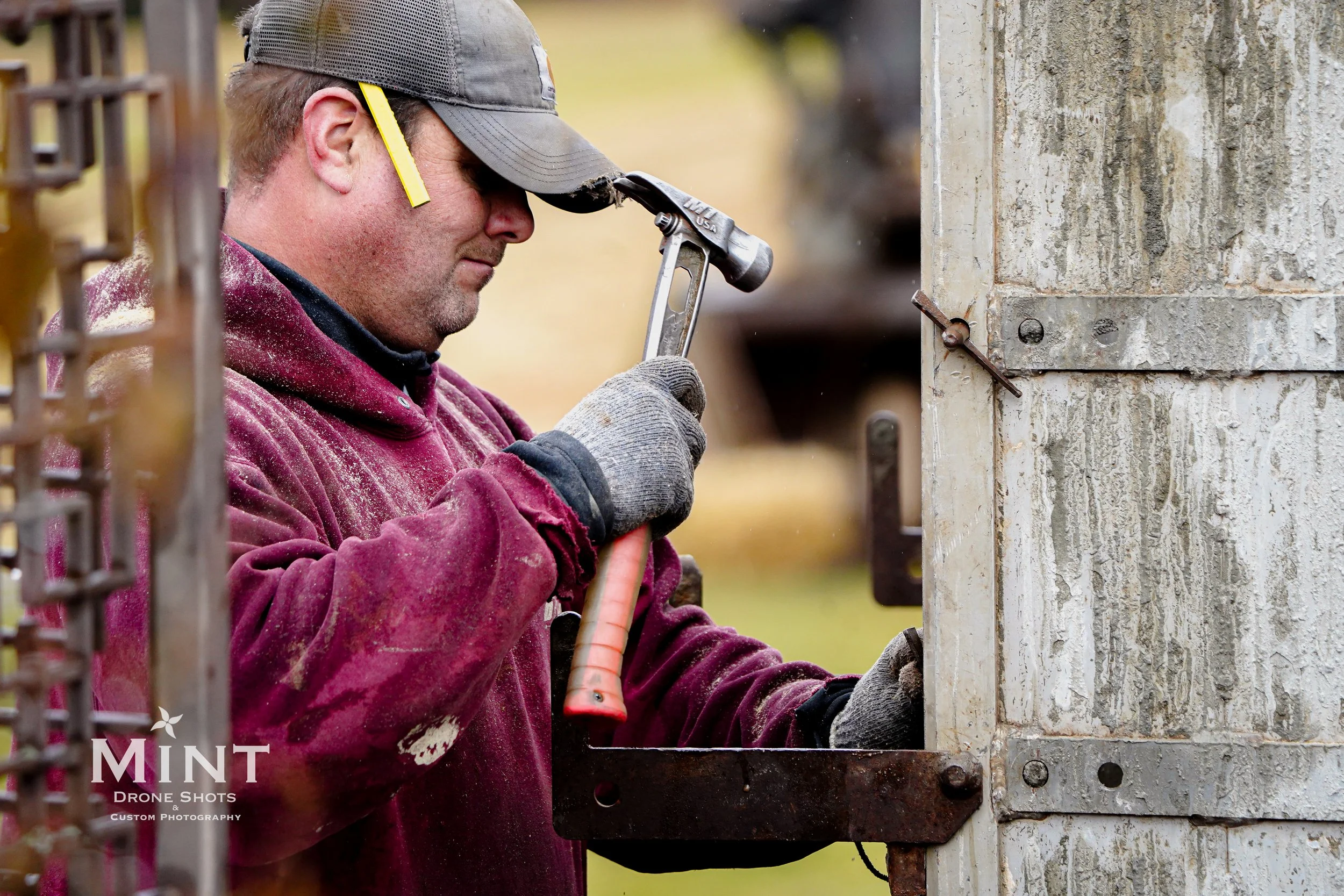 A person in a cap and glove using a hammer on a metal structure outdoors.