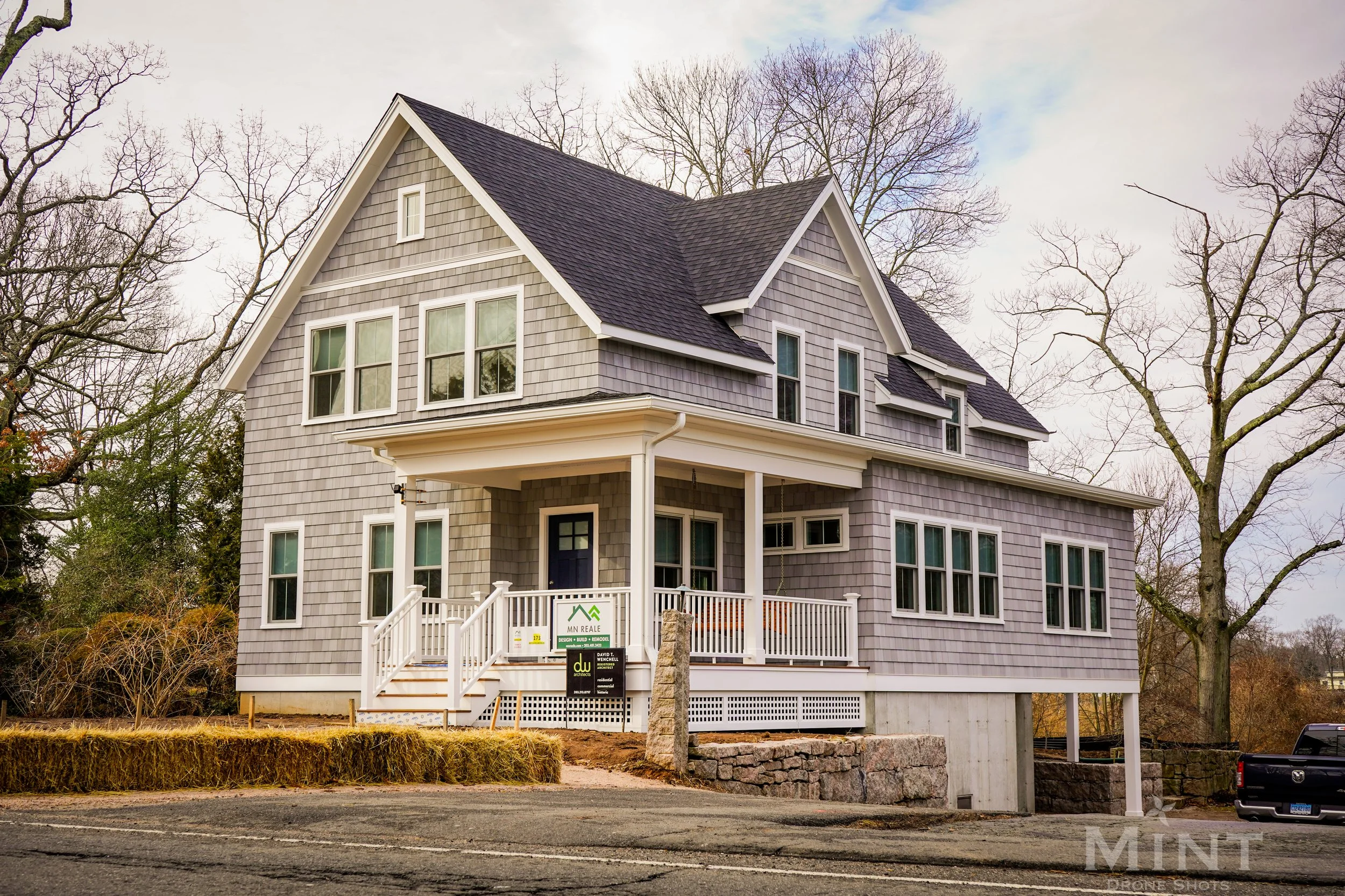 Two-story gray house with a gable roof and front porch, surrounded by bare trees and positioned on a slightly elevated foundation.