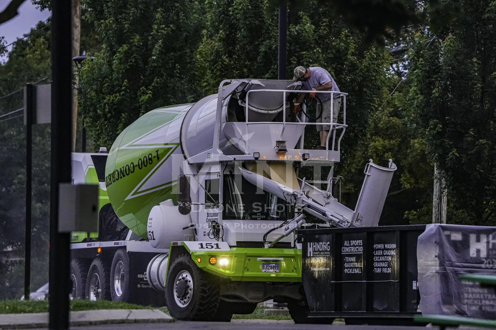A cement truck with a worker on top next to a construction site.