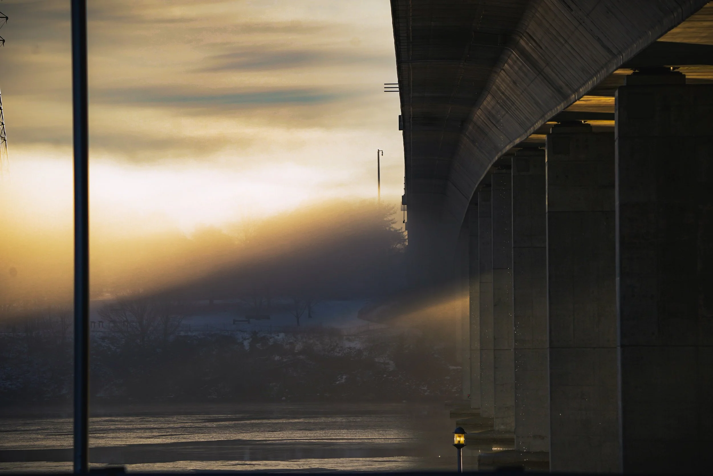 Sunlight filtering through fog under a bridge.