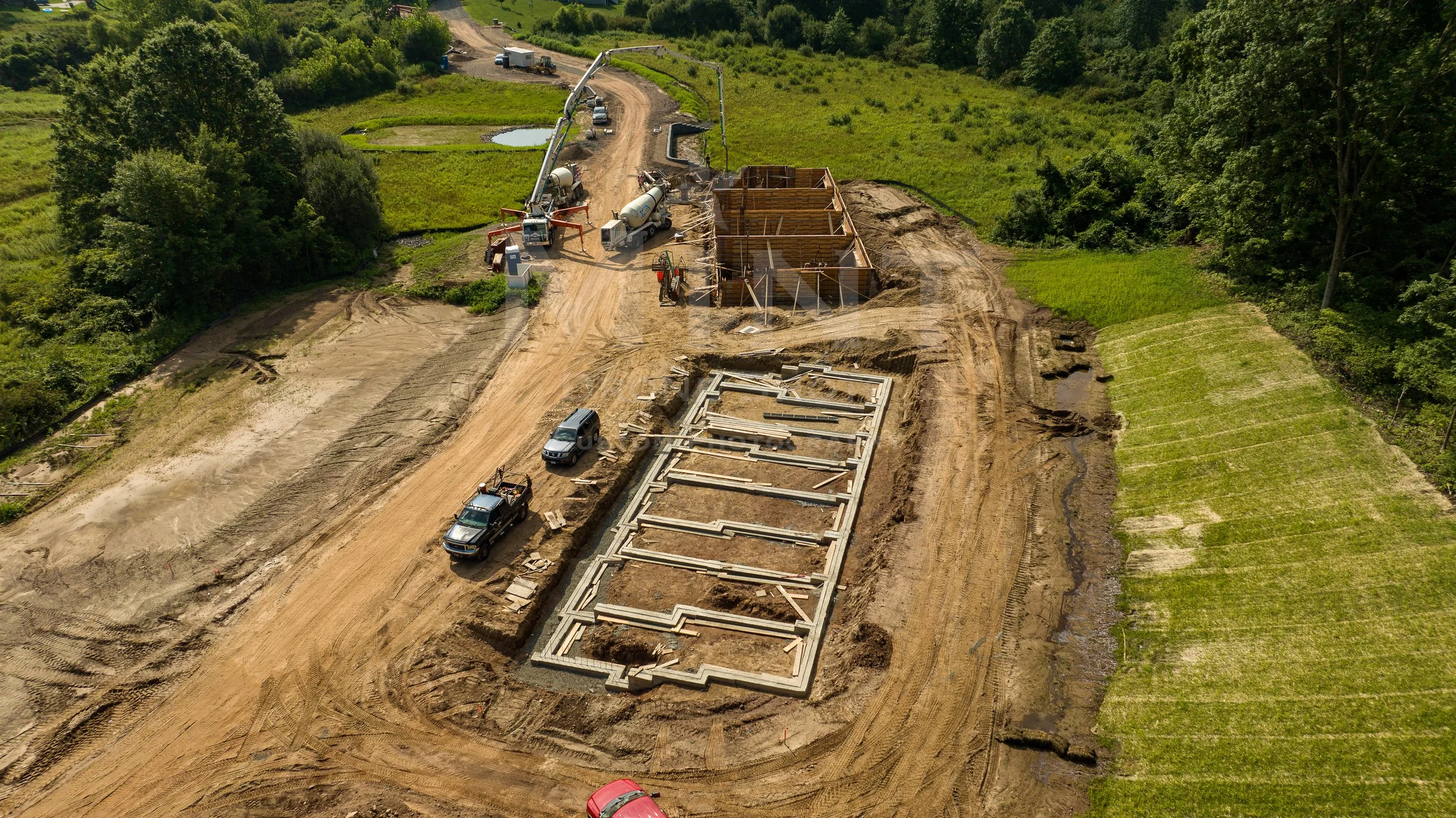 Aerial view of a construction site with a building foundation and surrounding forested landscape.