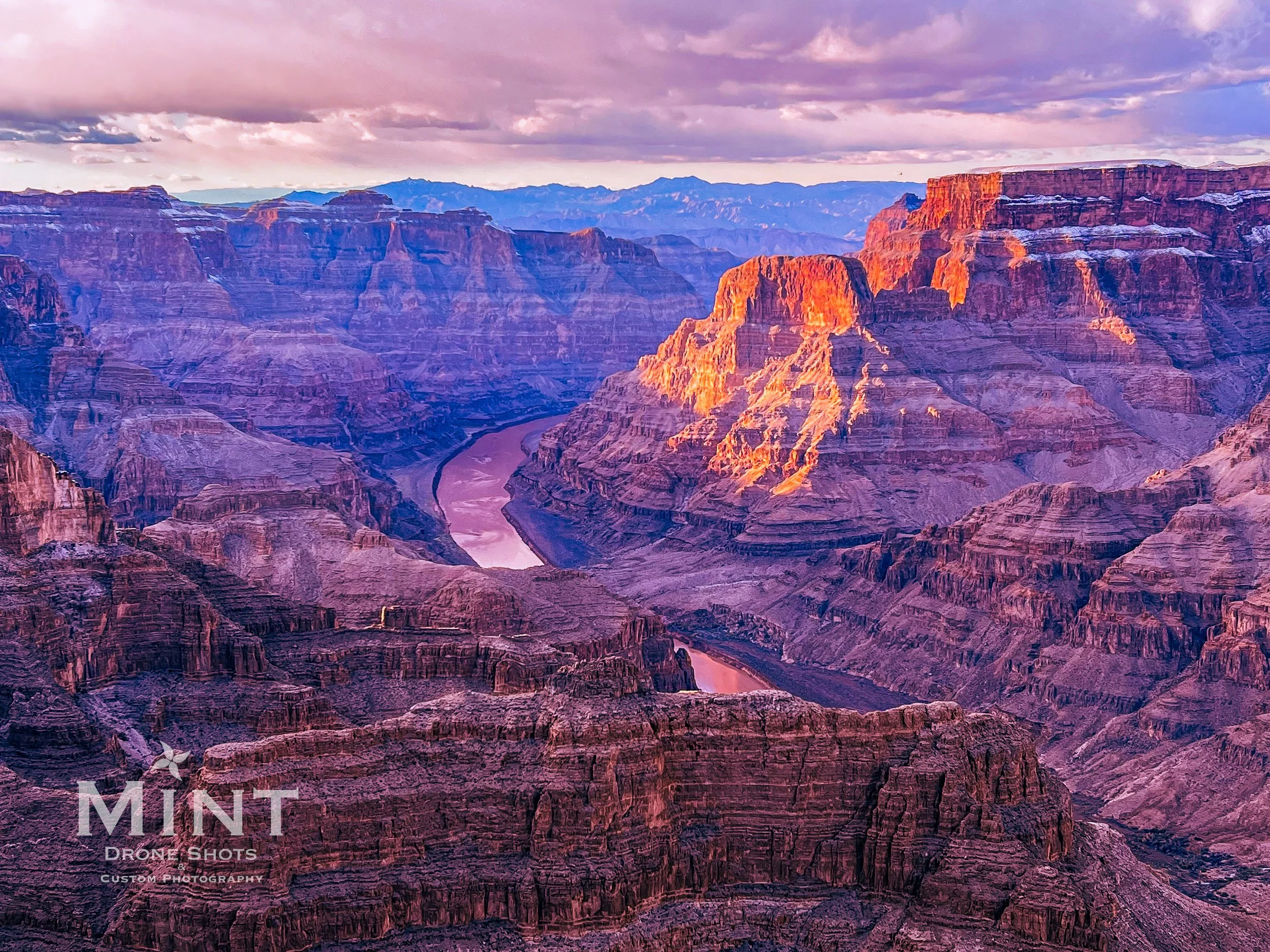 Aerial view of the Grand Canyon at sunset with dramatic shadows on rock formations and the Colorado River below.