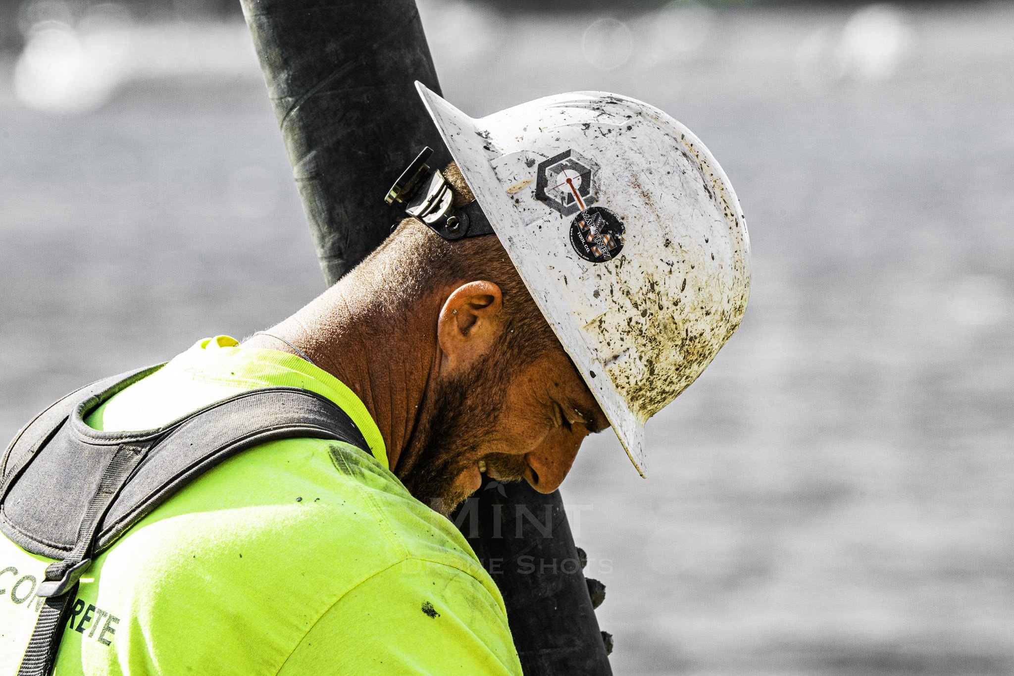 Construction worker wearing a dirty hard hat and fluorescent shirt, holding a large black pipe.