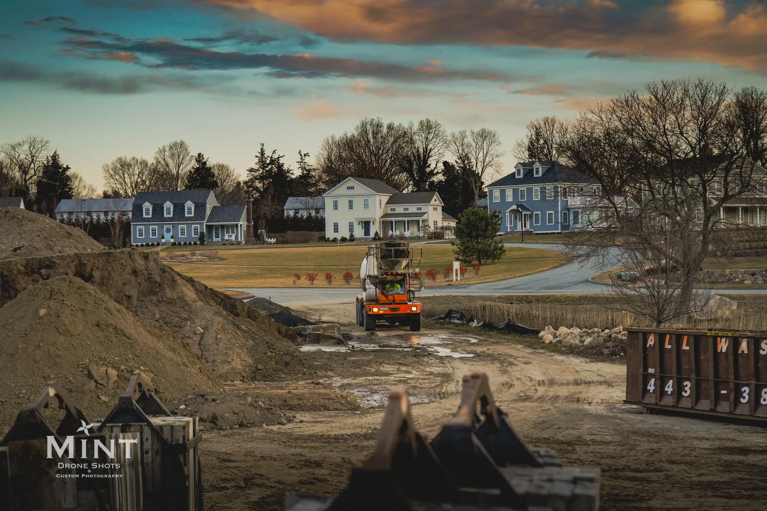 Construction site with a dump truck and traditional houses in the background at sunset.