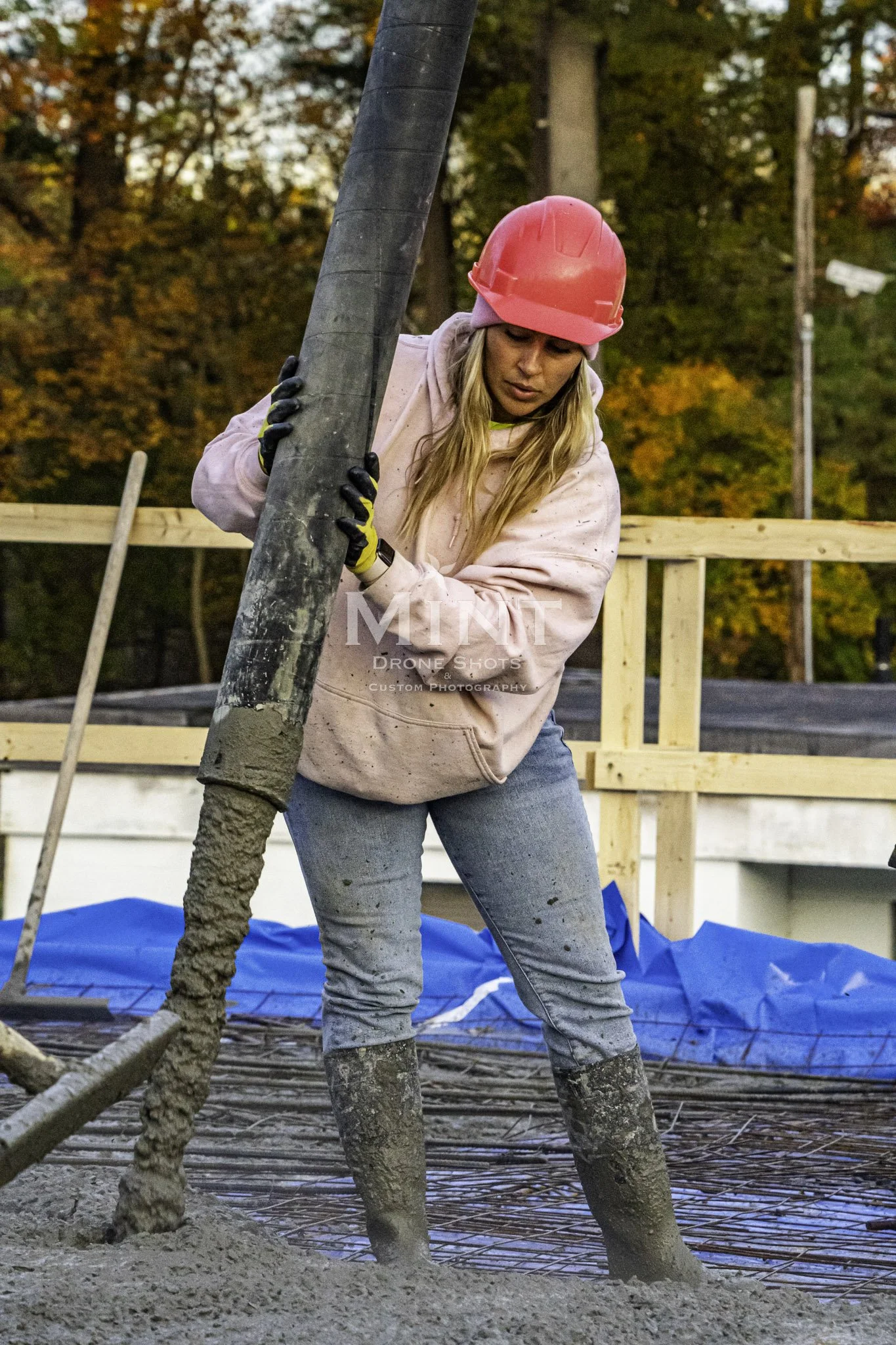 A woman wearing a pink hard hat and hoodie operates a concrete pump on a construction site.