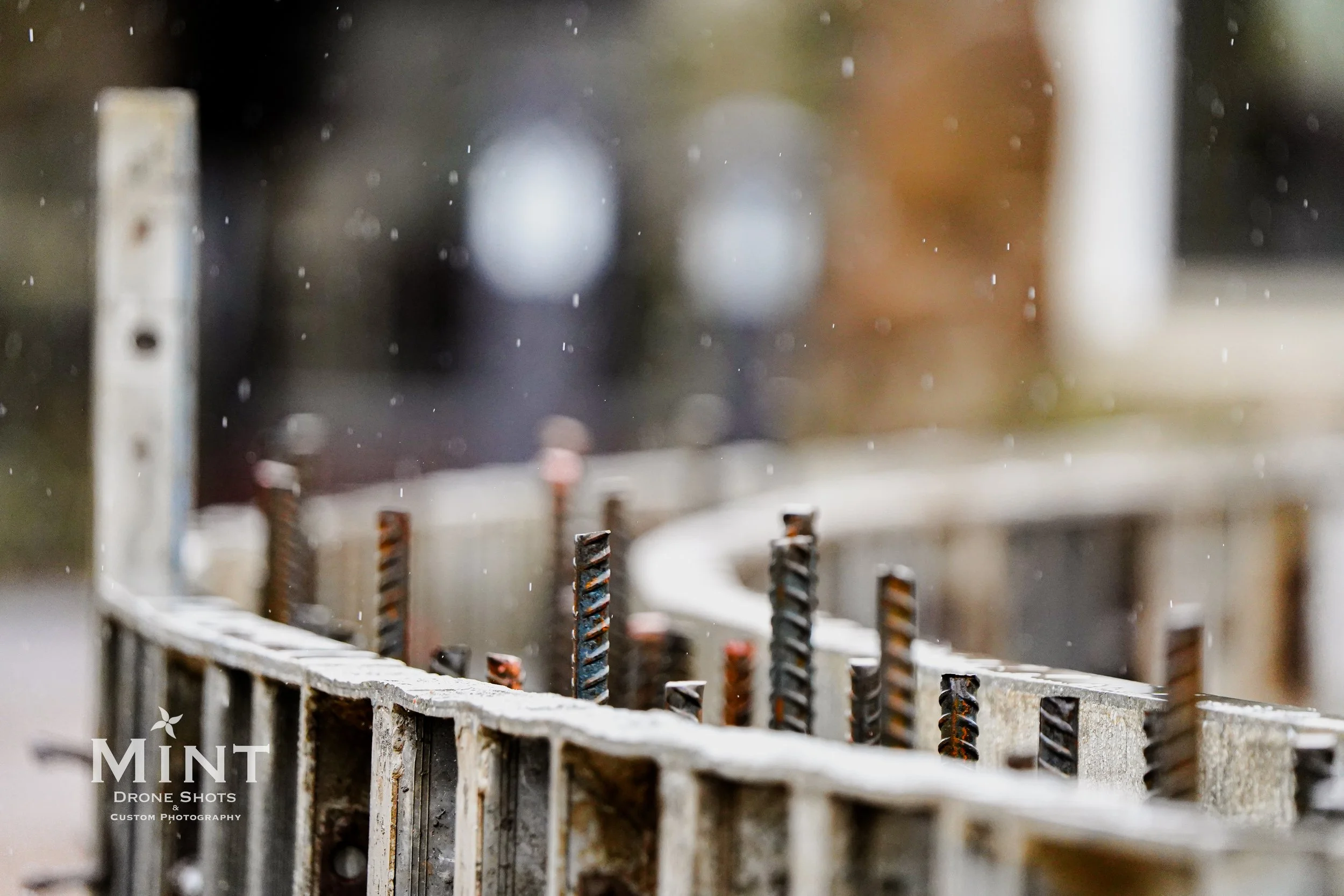 Close-up of a concrete construction site with rebar protruding from a formwork in rainy weather.