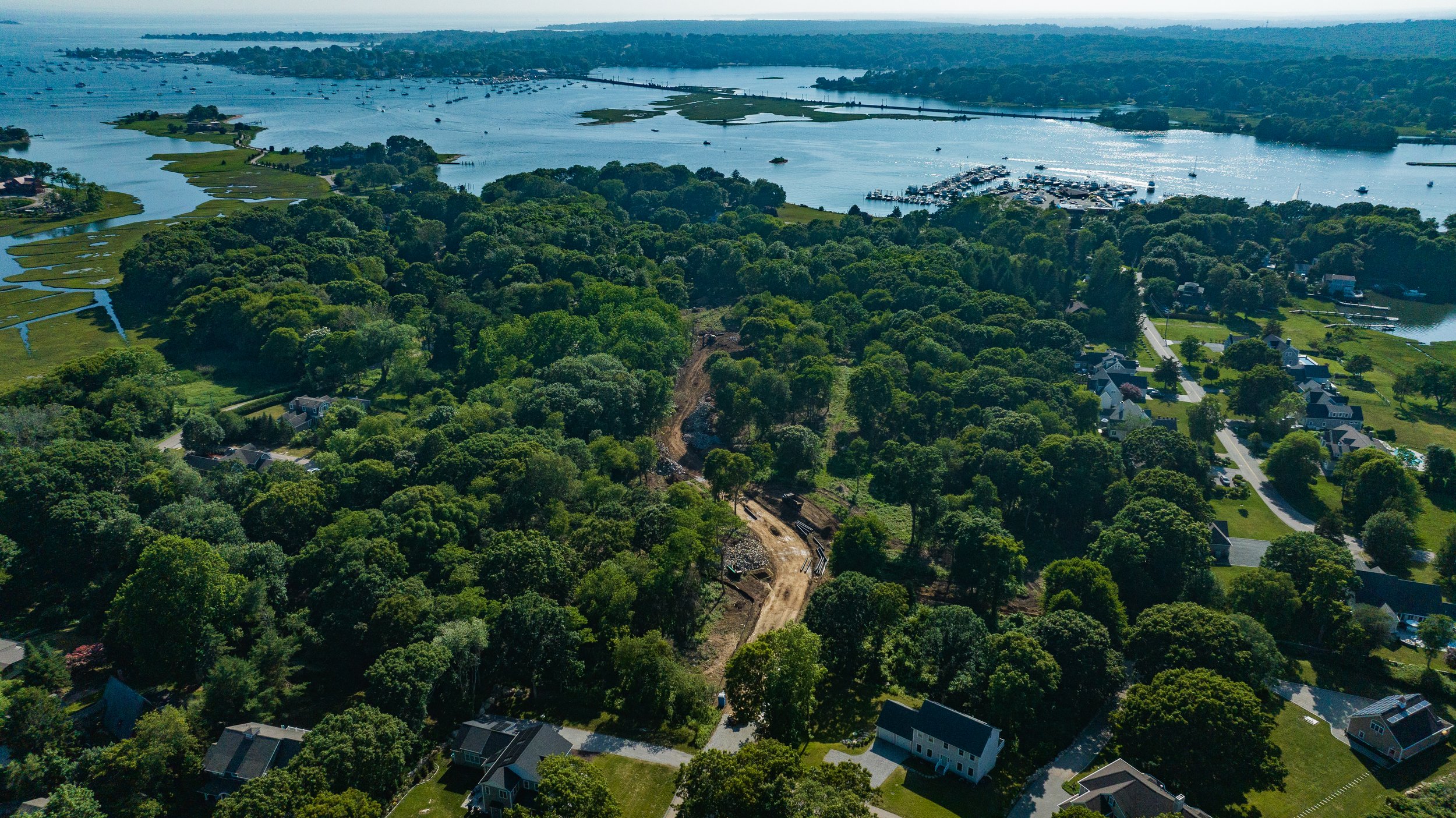 Aerial view of a forested coastal area with scattered houses and a waterway with boats.