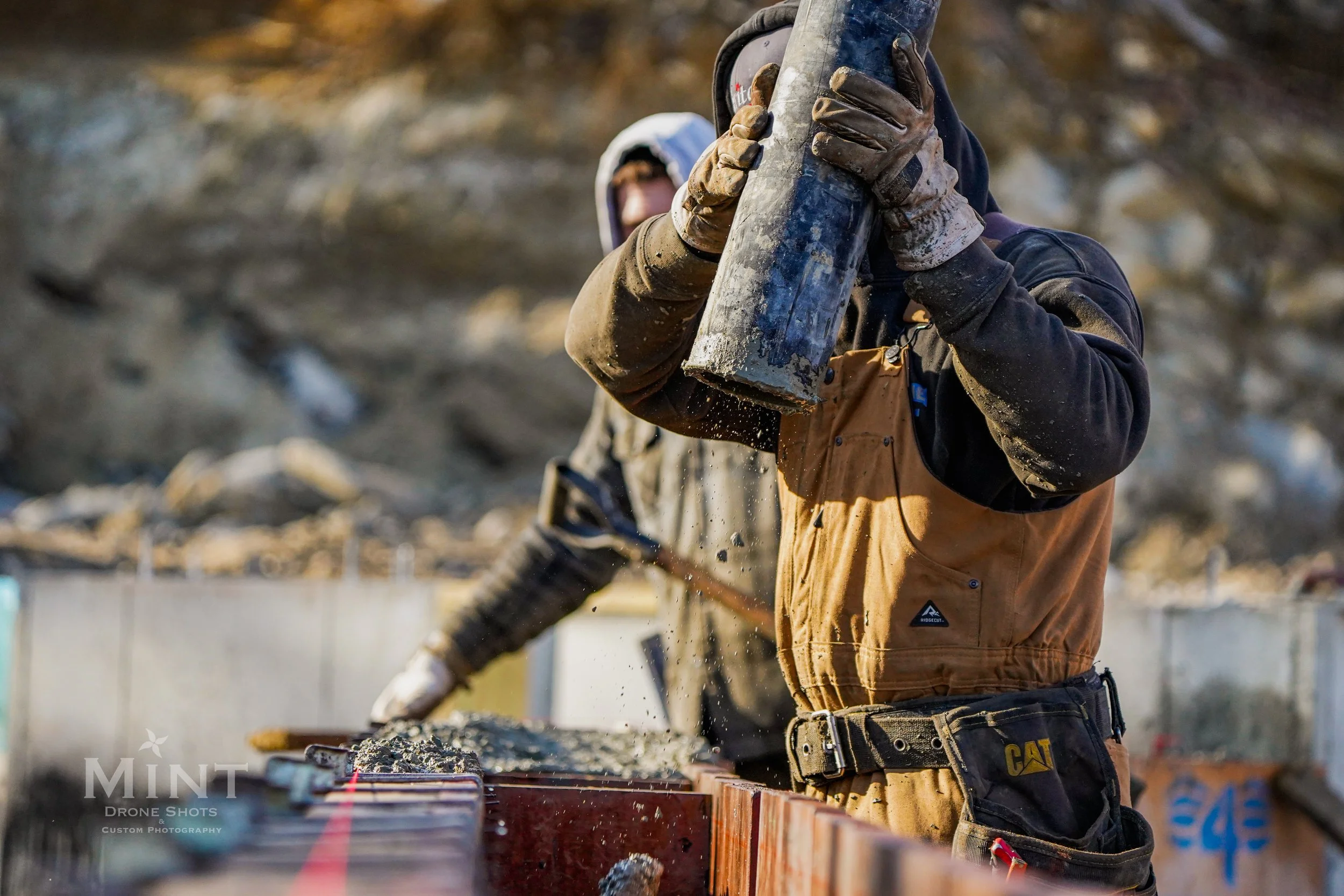 Construction worker pouring concrete into a mold at a construction site, wearing gloves and protective clothing.
