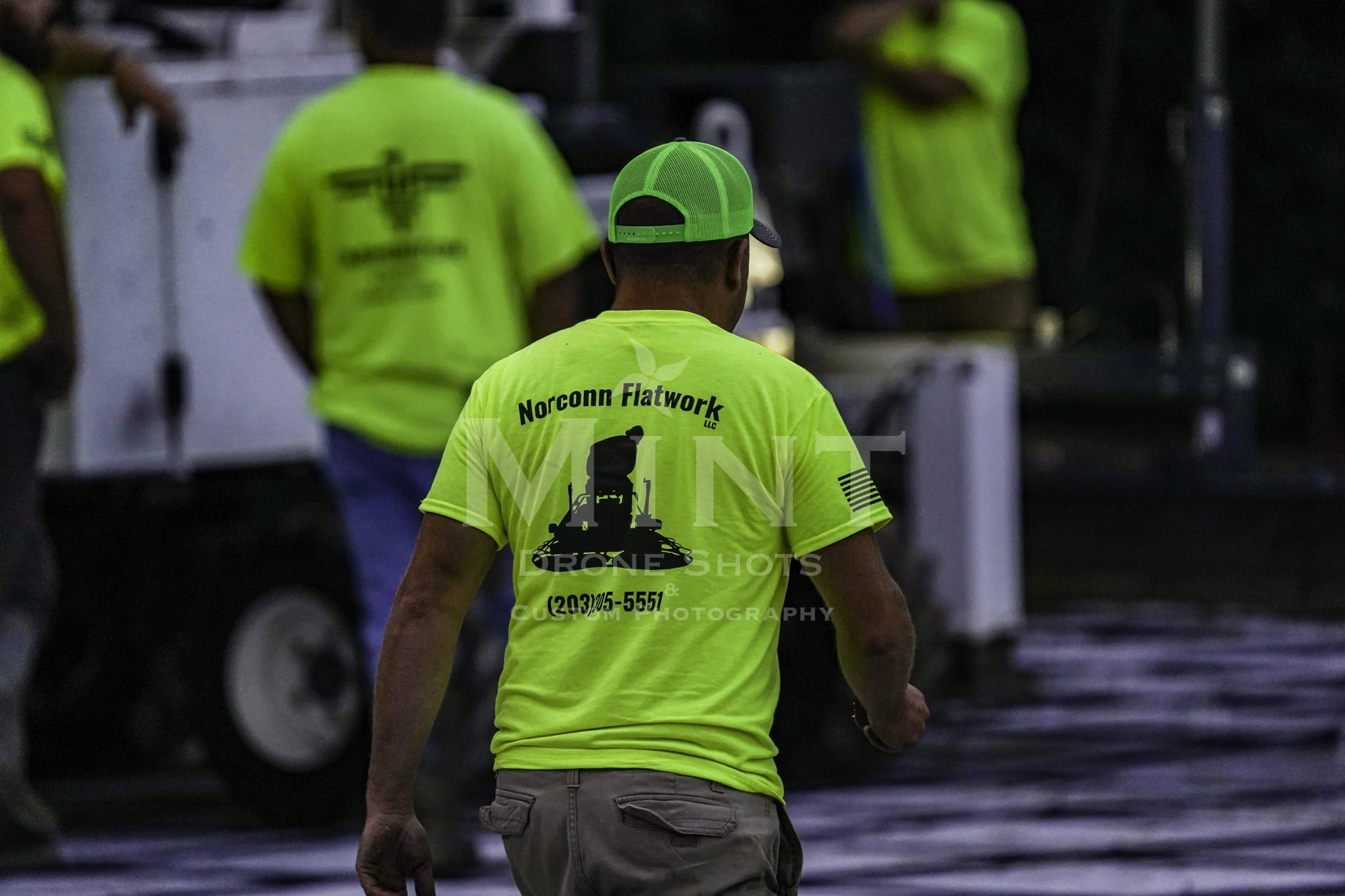 Workers in yellow shirts with Norconn Flatwork logo engaged in construction site activities.