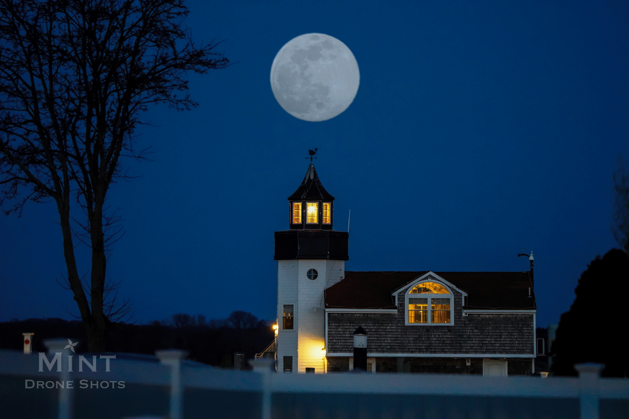 Night view of a lighthouse with a bright moon and glowing windows.