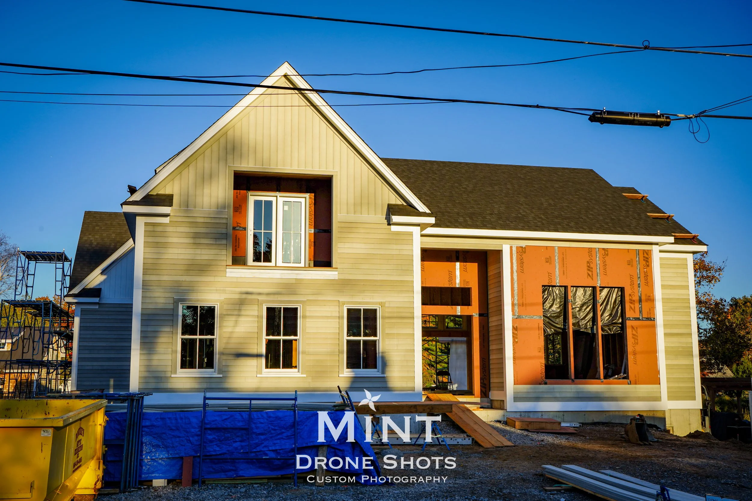 Partially constructed house with beige siding and a black roof, surrounded by construction materials and scaffolding.