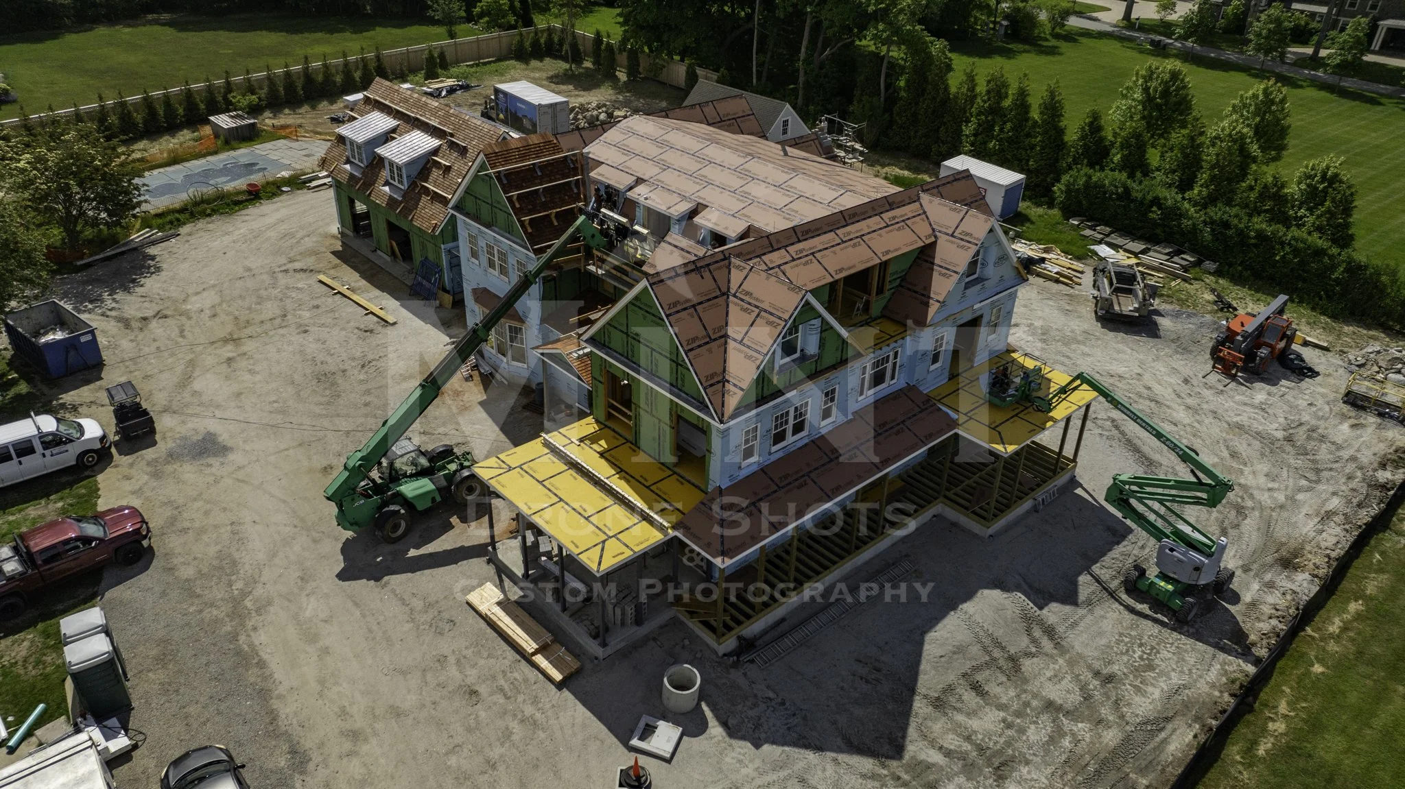 Aerial view of a house under construction with cranes and building materials on site, surrounded by trees.