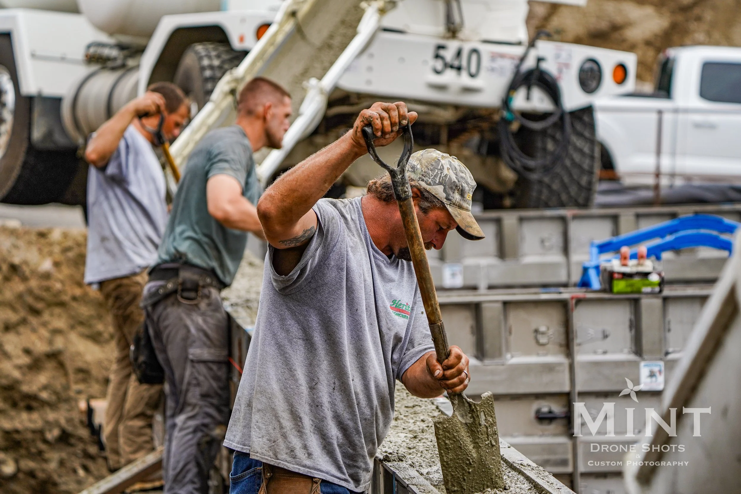 Construction workers pouring concrete from a cement mixer into a formwork at a construction site, using shovels.