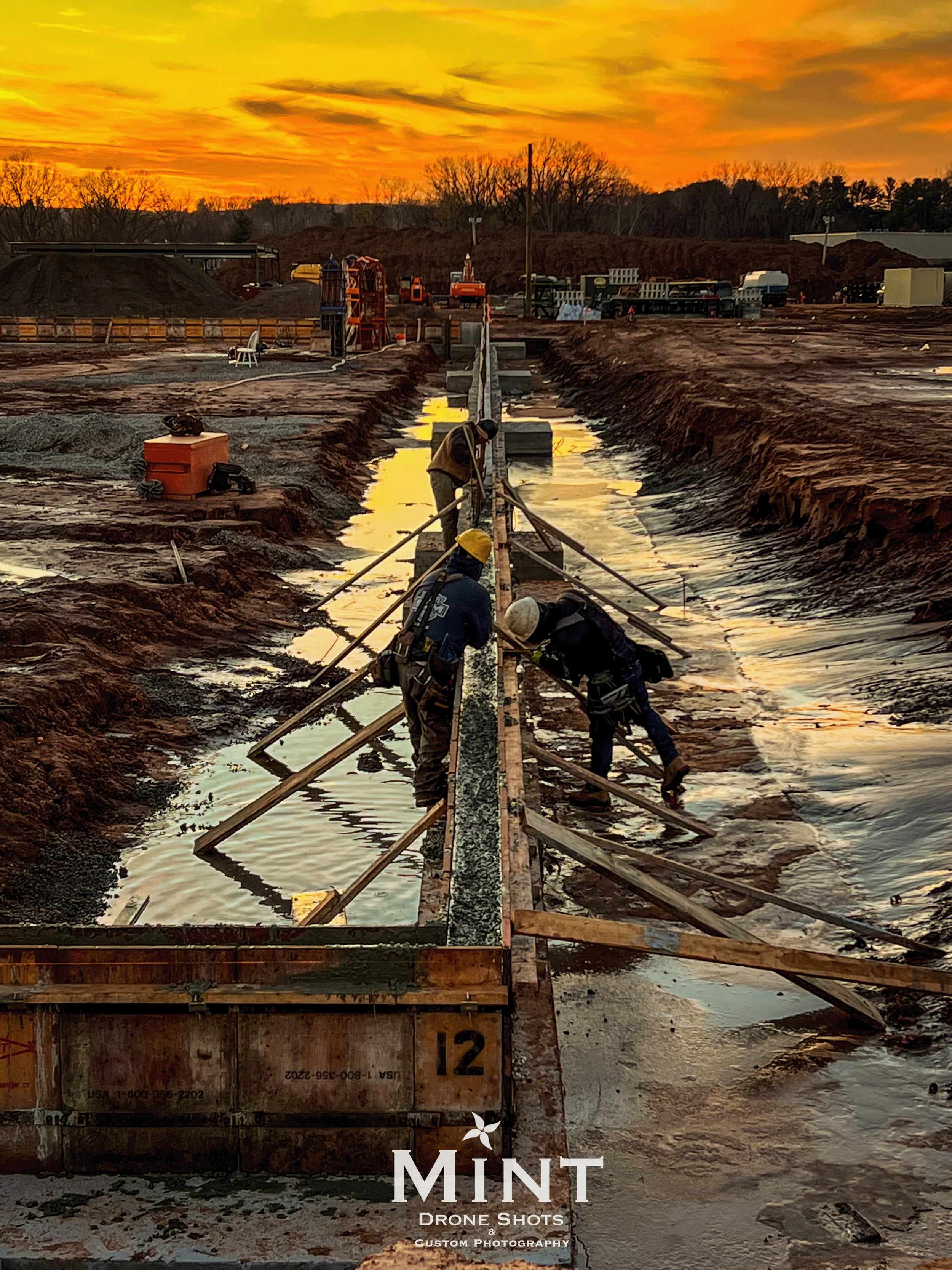 Construction site at sunset with workers pouring concrete.