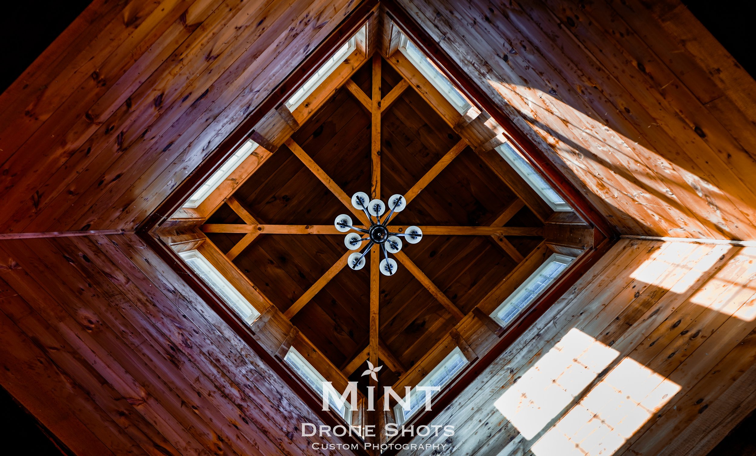 Interior view of a wooden ceiling with a geometric design and a modern chandelier at the center.