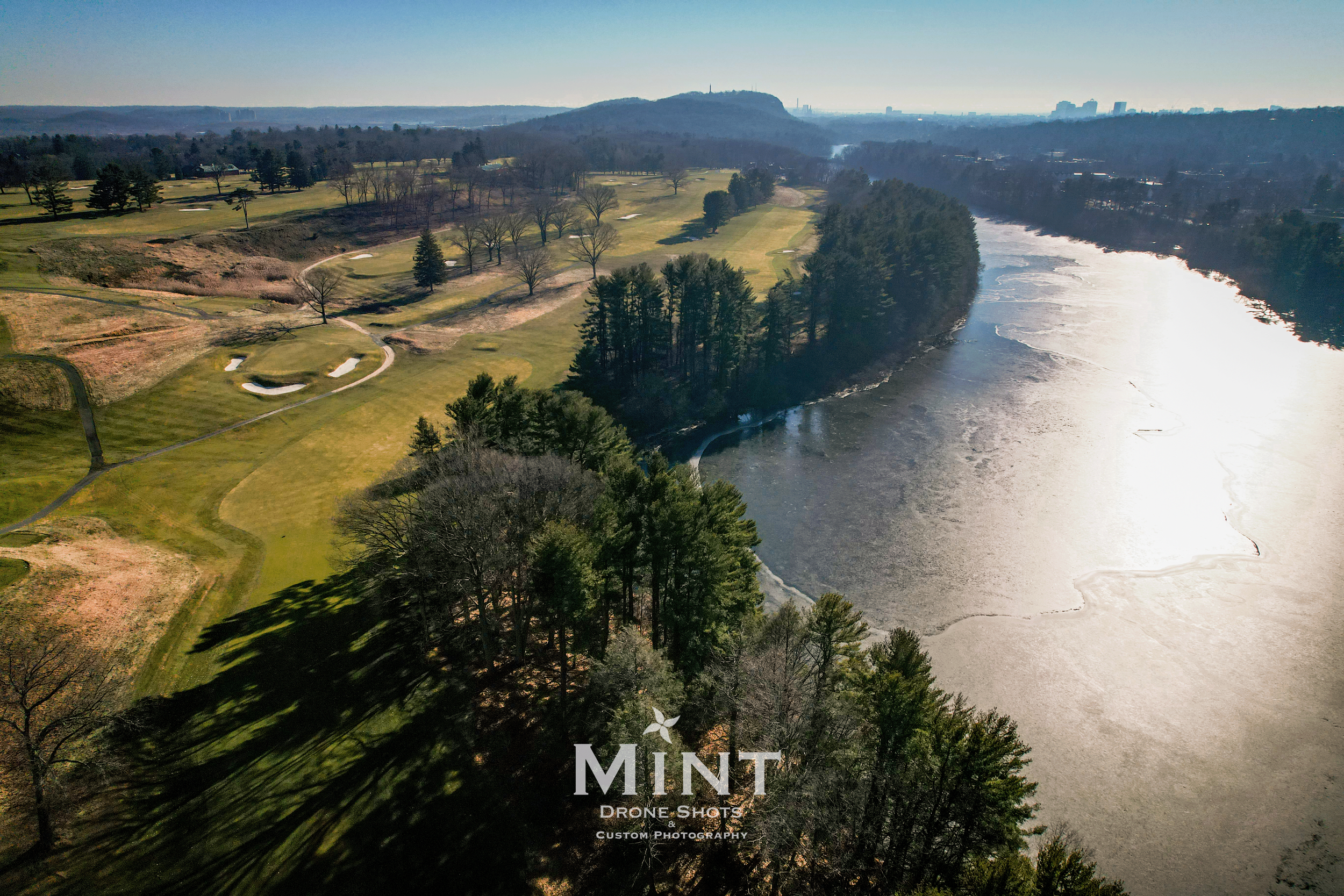 Aerial view of a golf course next to a river surrounded by trees and landscape.