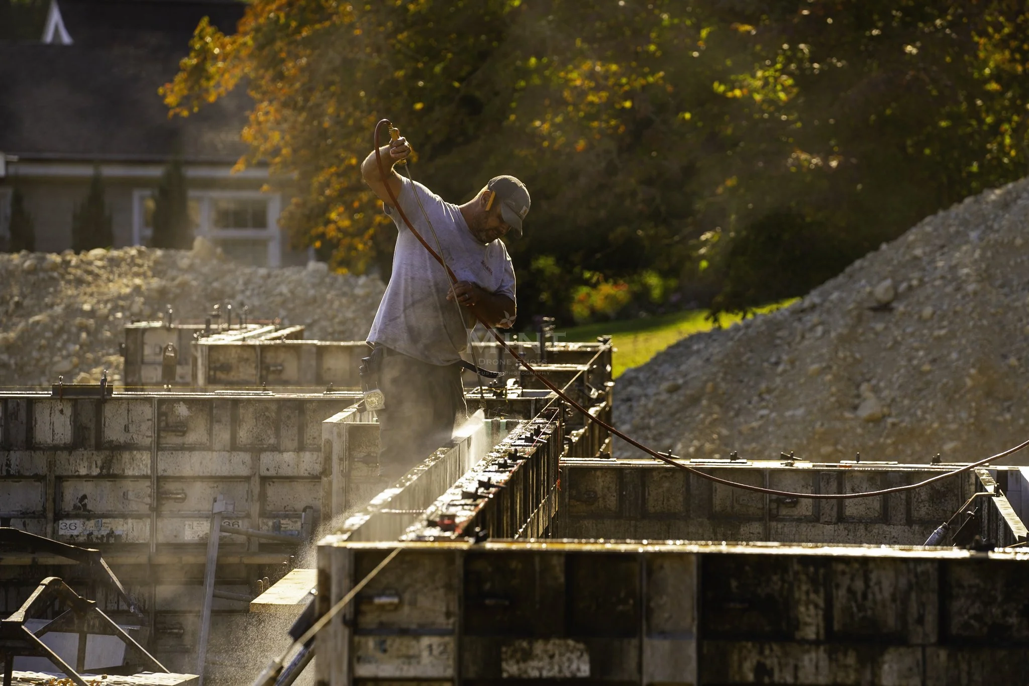 Construction worker cleaning metal framework with pressure washer at a construction site.