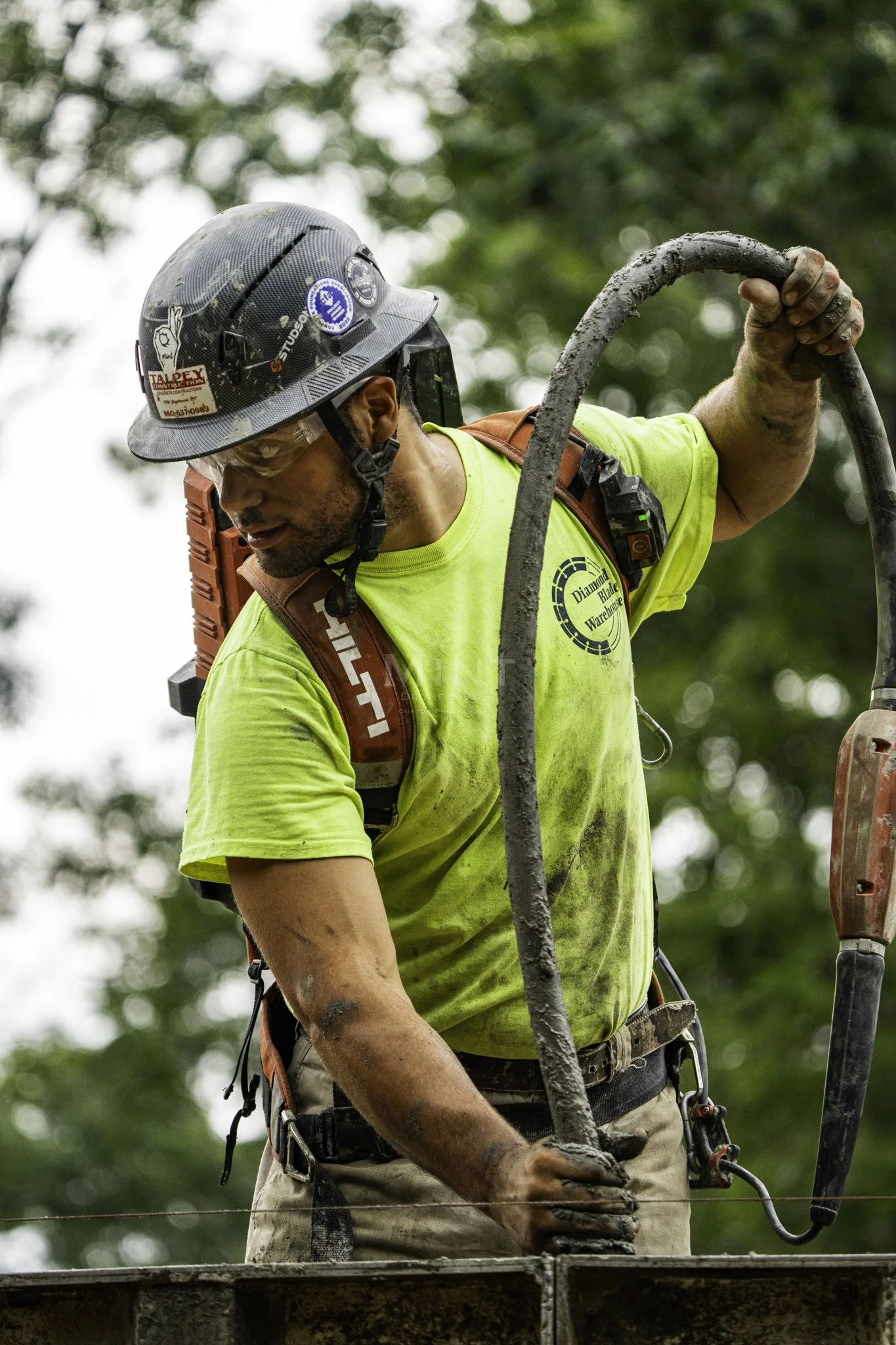 Construction worker wearing a hard hat and neon shirt, holding a concrete hose.
