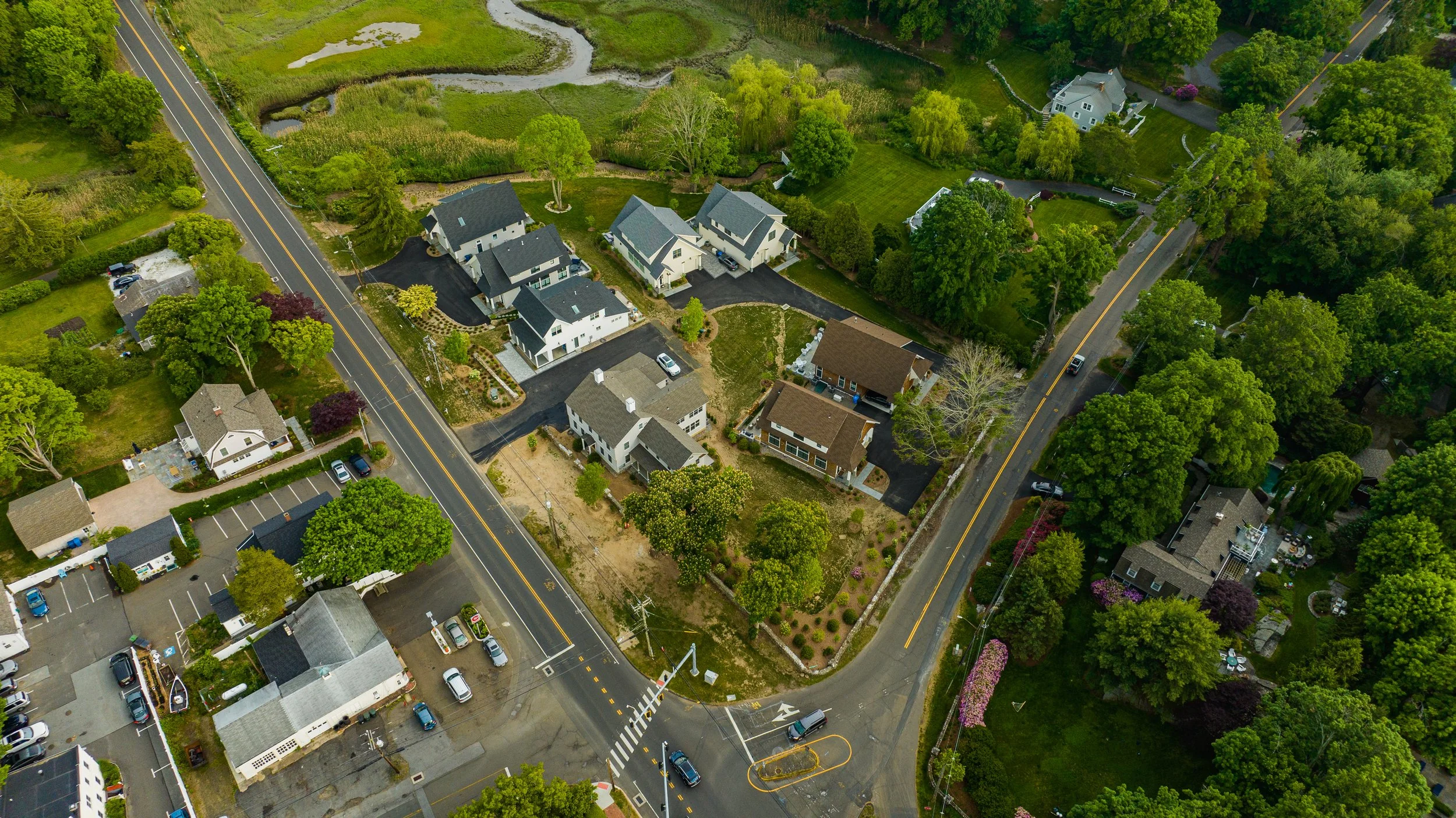 Aerial view of a suburban neighborhood with houses, roads, greenery, and a parking lot.