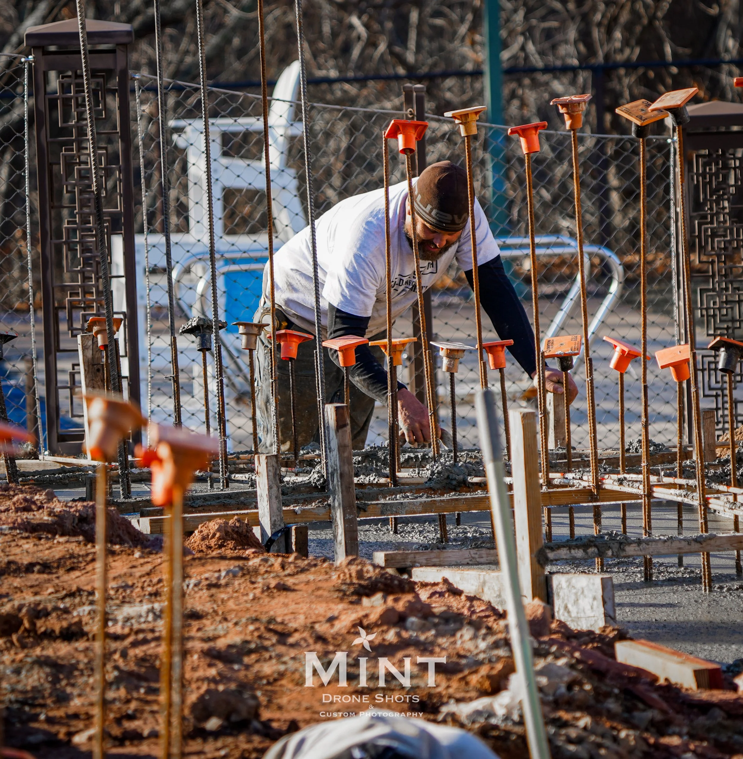 Construction worker pouring concrete and installing rebar at a construction site with metal rods and orange safety caps.