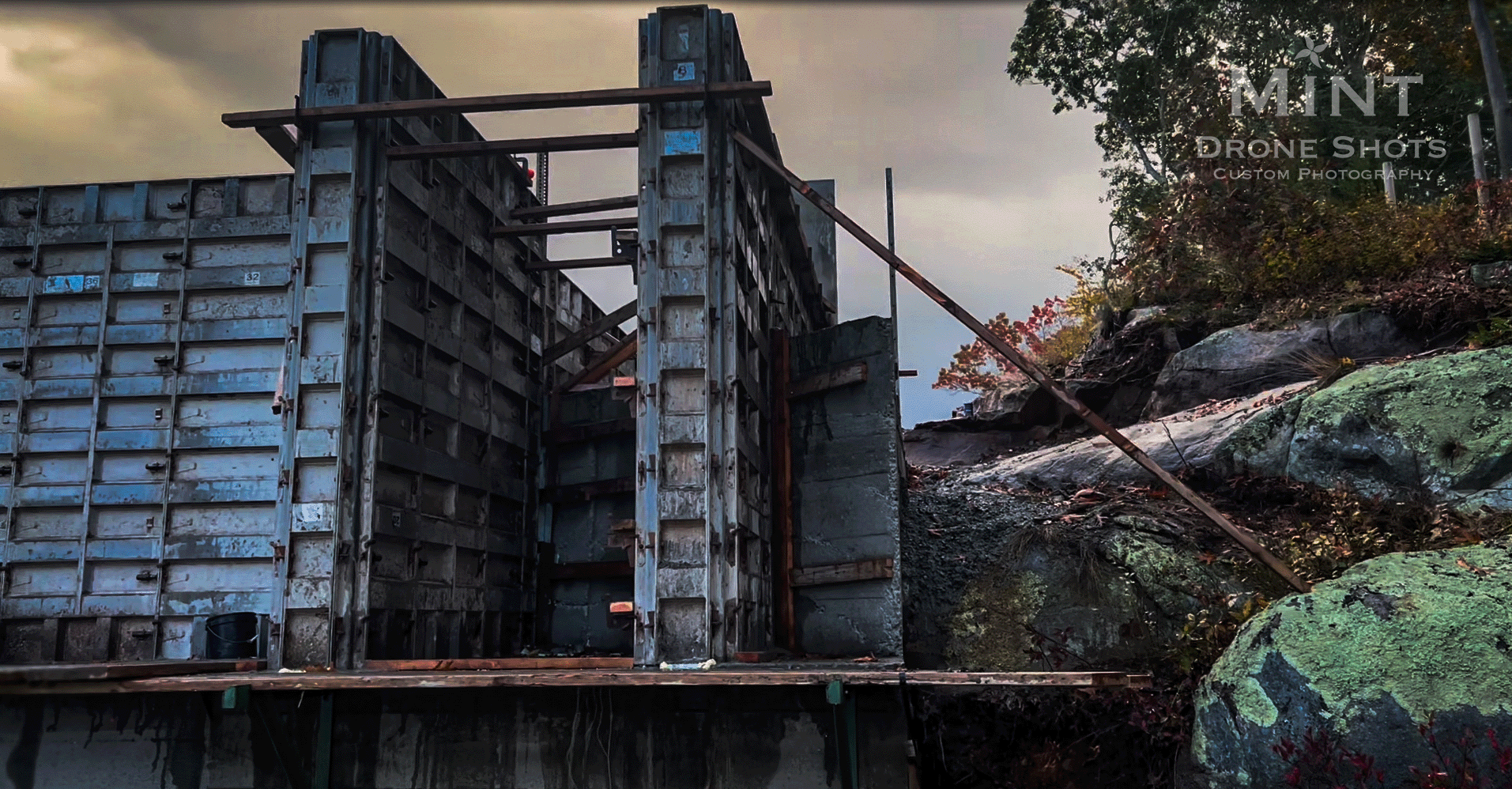 Construction site with concrete forms set up against a rocky hillside with trees.