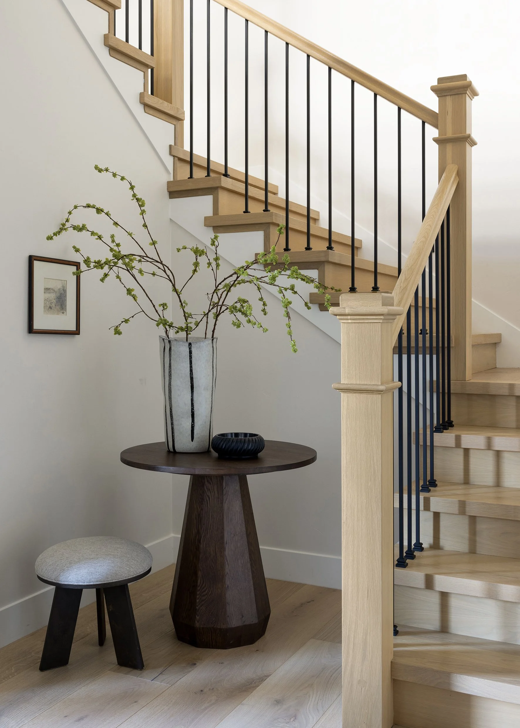 This custom staircase design blends modern lines with warm natural materials to create a welcoming and timeless entry experience. Light oak wood treads and handrails are paired with clean black iron balusters for a refined contrast, while soft neutra