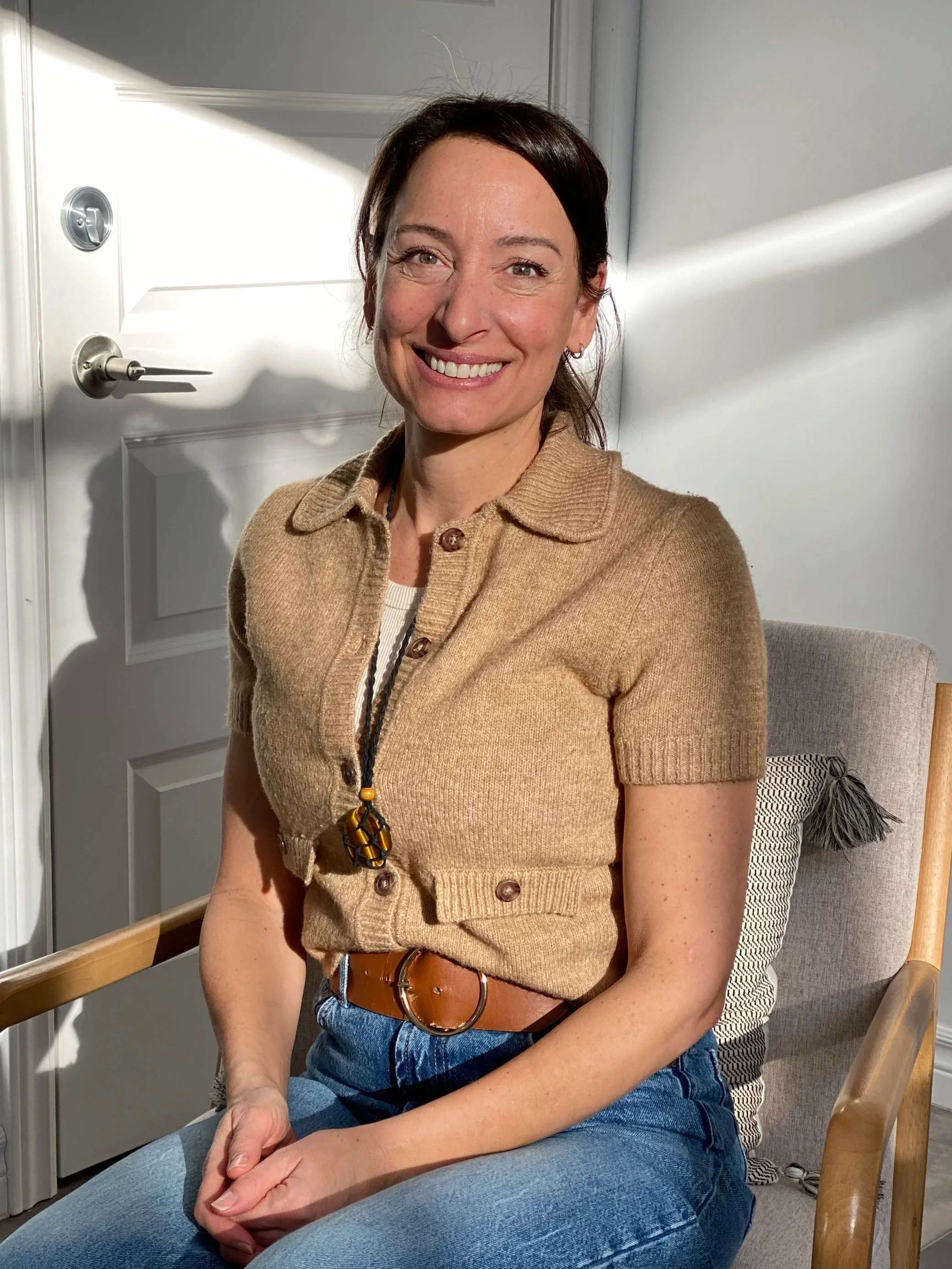 une femme souriante est assise dans un fauteuil éclairée par le soleil