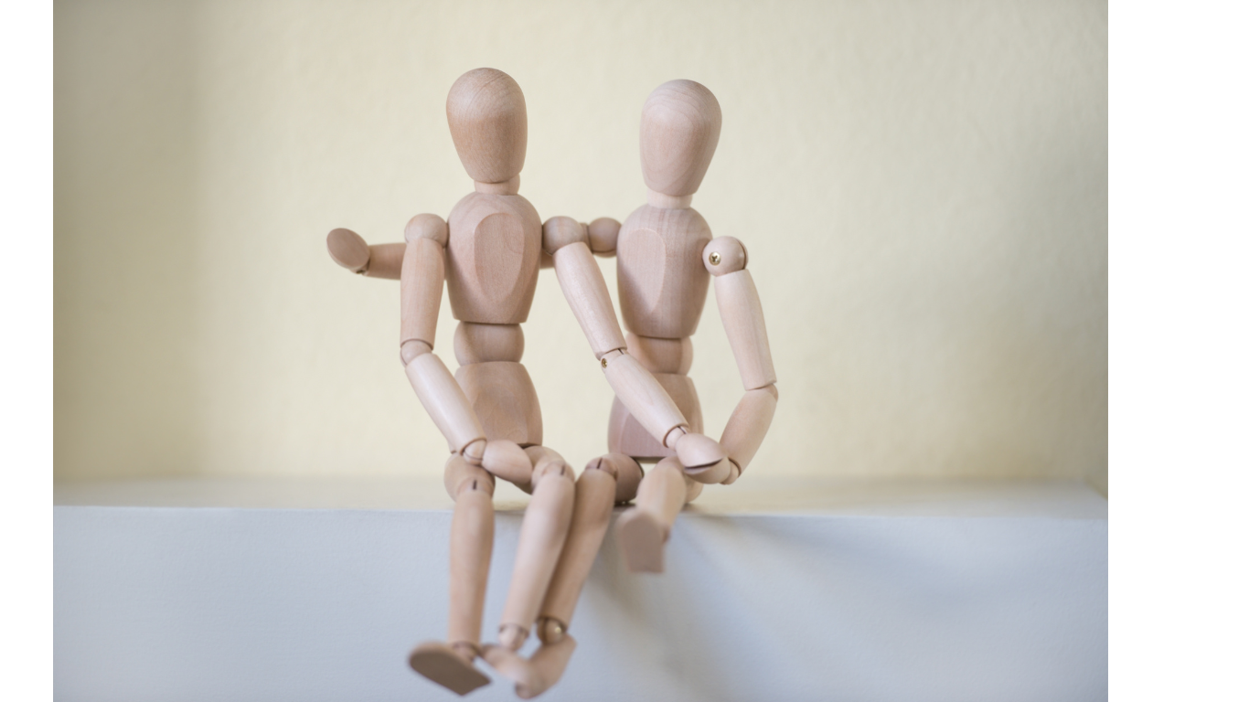 Two wooden drawing models posed in a warm embrace to represent the compassionate approach to art therapy Fresh Therapy LLC offers.