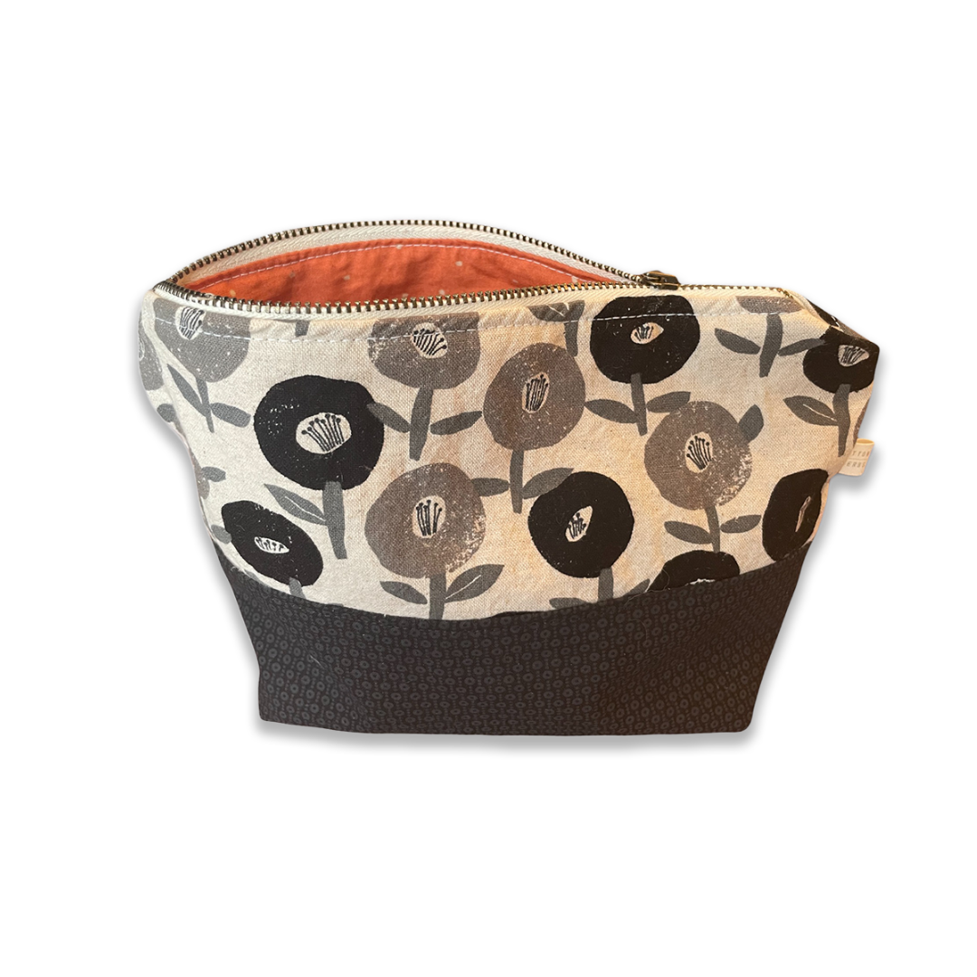 Fabric zippered pouch with black and gray flower pattern on white background and a black bottom section, partially open showing a salmon-colored interior.