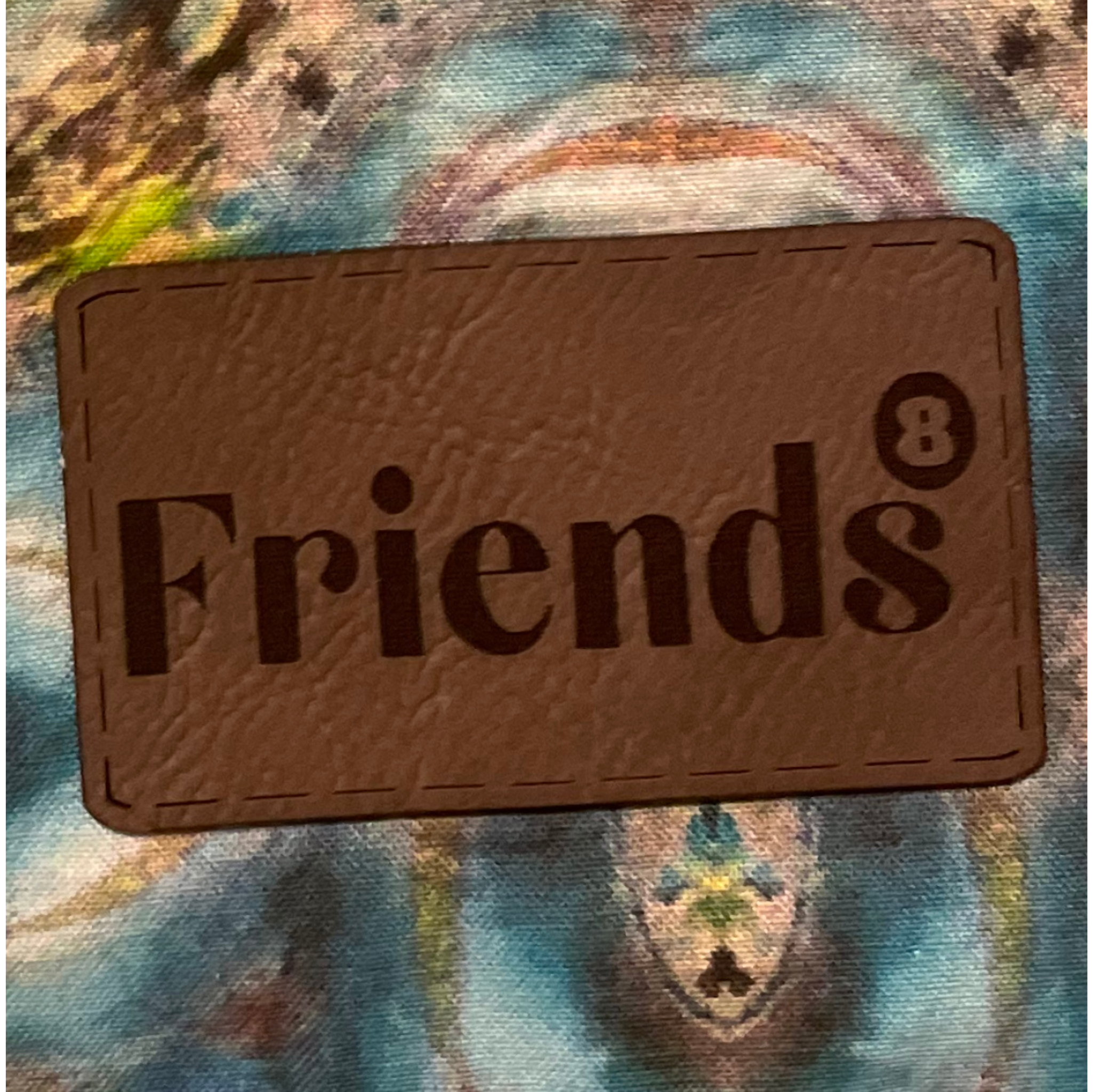 A textured brown Nike shoe tag with the word 'friends' and the number 8 printed on it, on top of a colorful, abstract background.