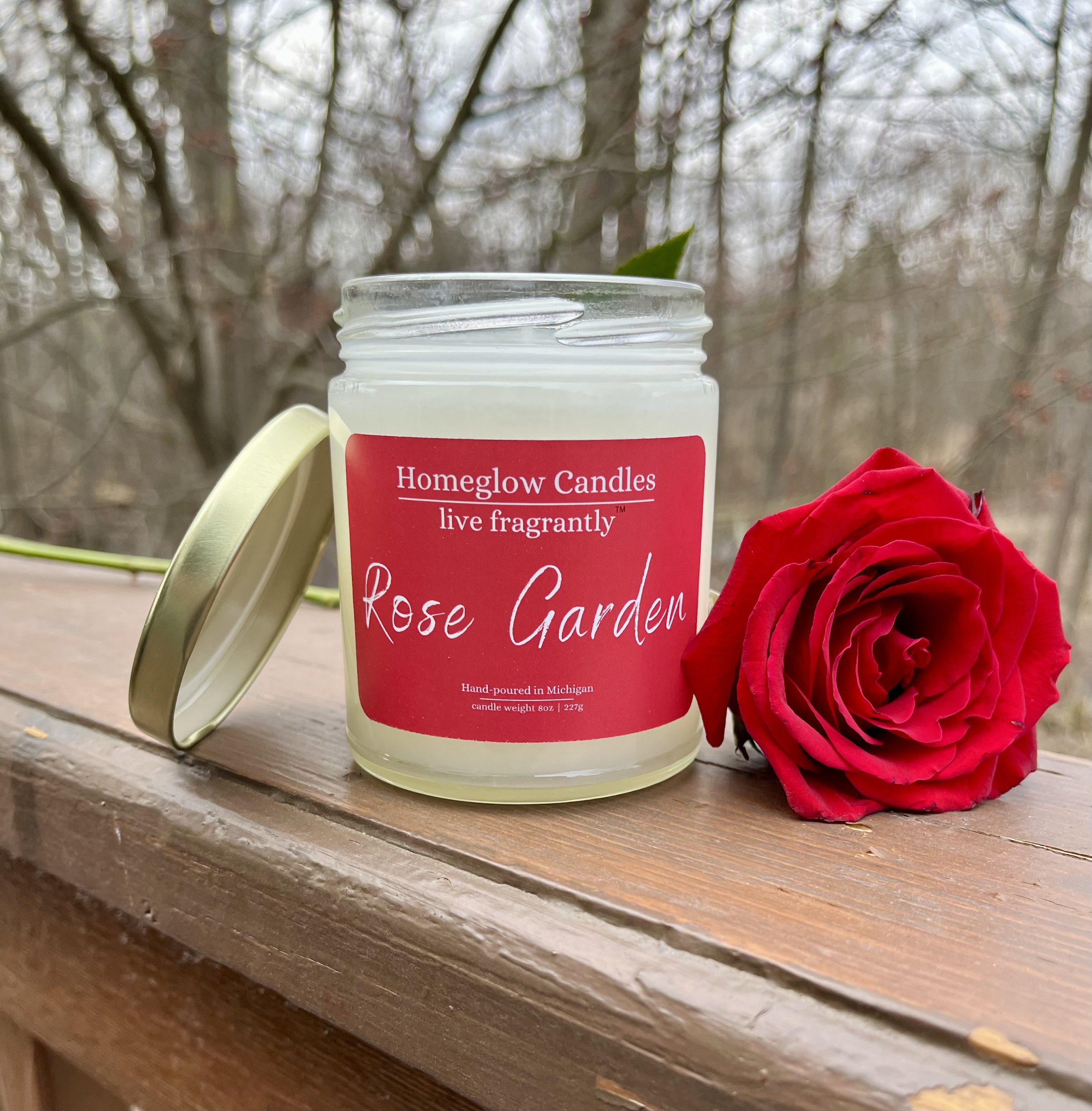 Rose Garden Candle by Homeglow Candles outside a ledge with a rose