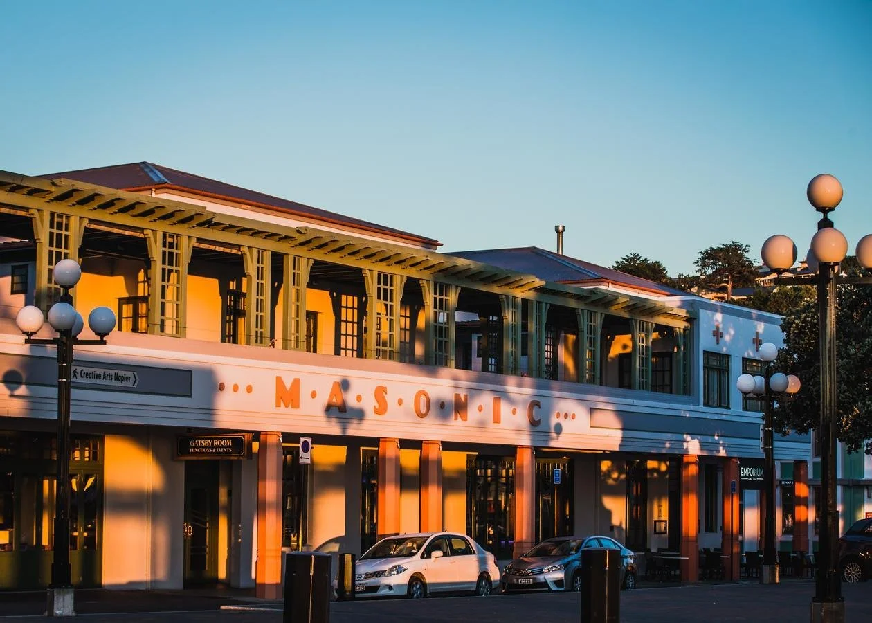 The Masonic building with a sign, surrounded by parked cars and street lamps during sunset.