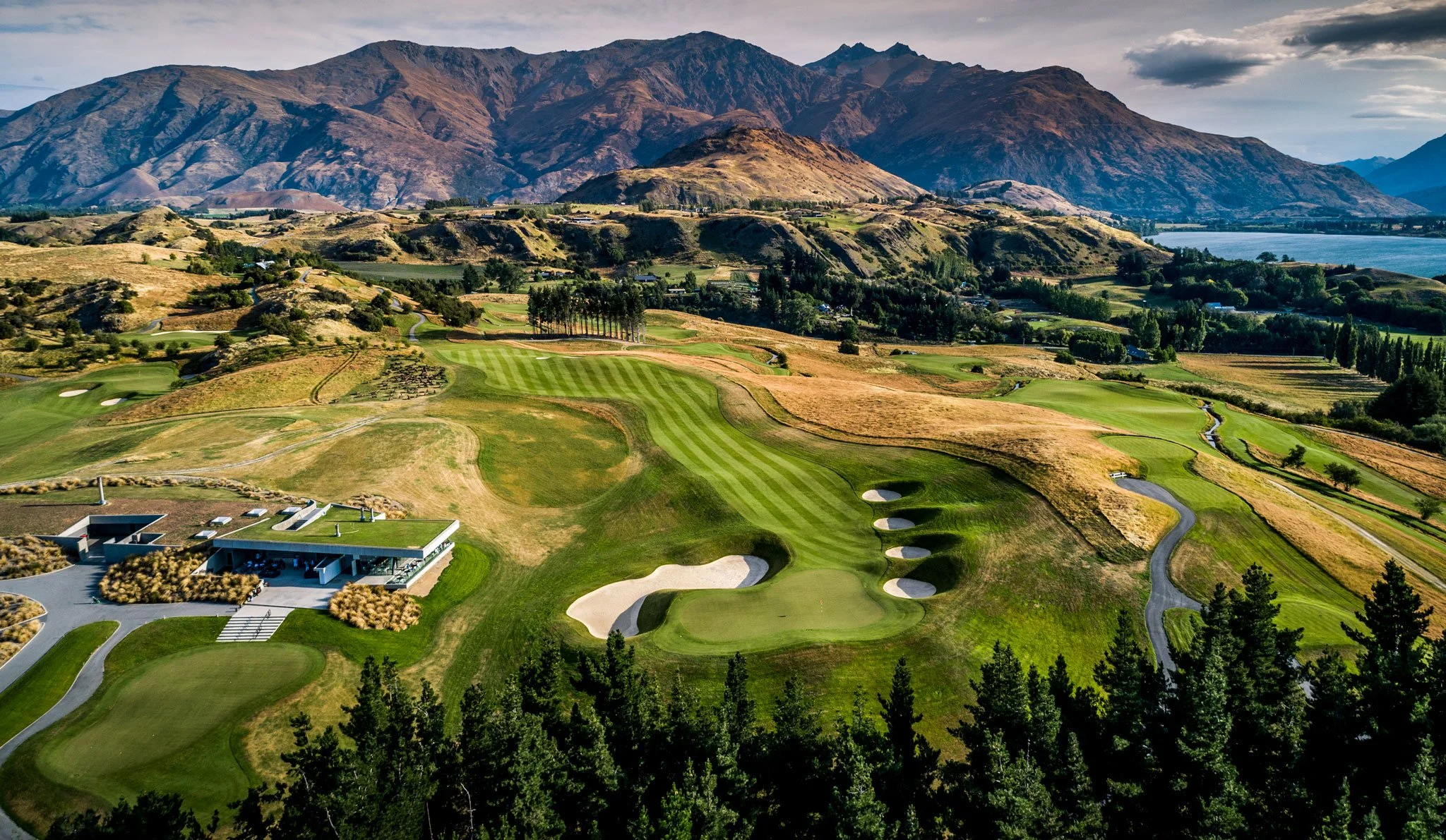 A scenic landscape of a golf course surrounded by rolling hills and mountains in the background, with a club house visible in the foreground.