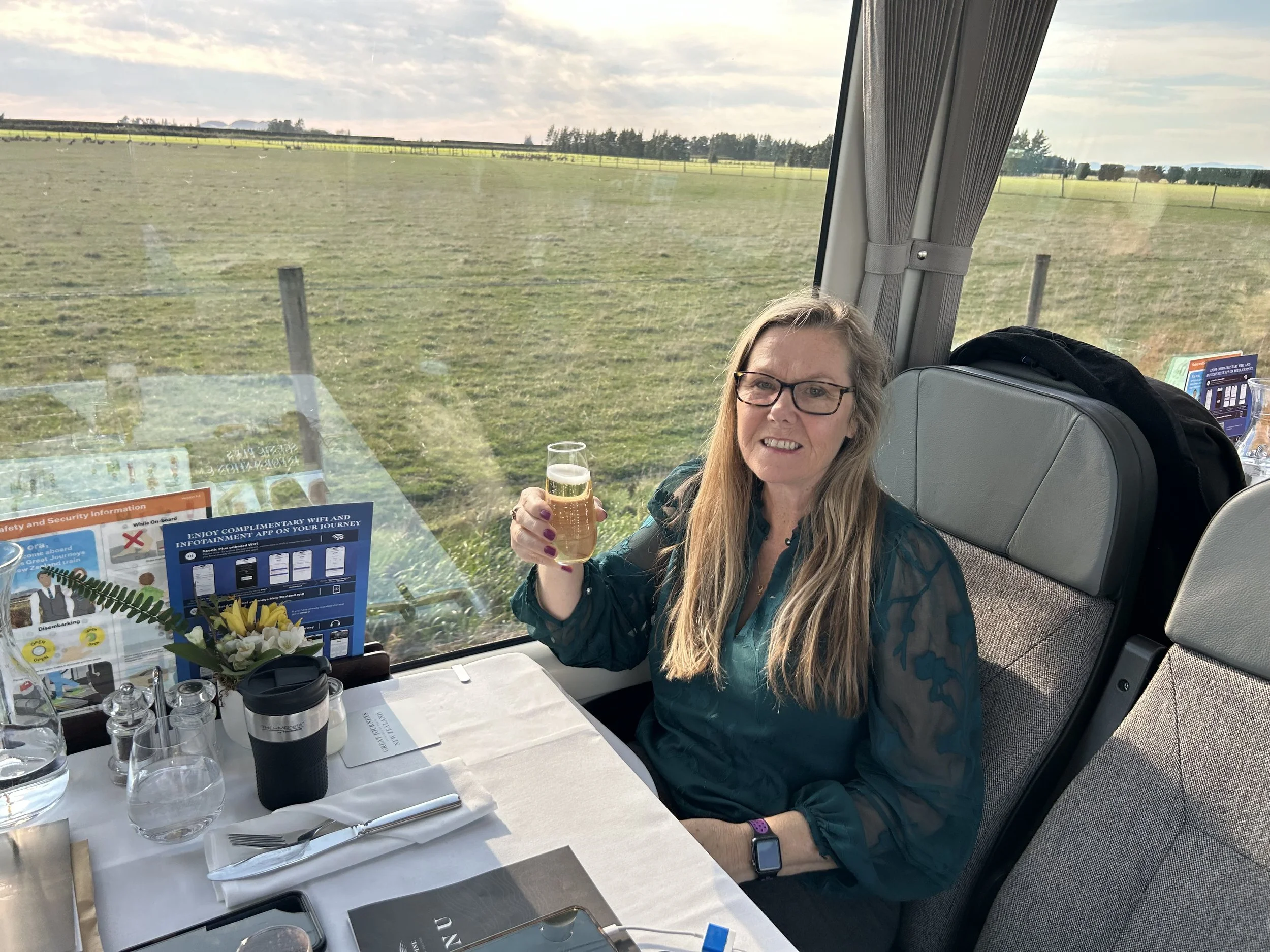 Holding a glass of champagne, while on the TransAlpine Scenic Plus train.