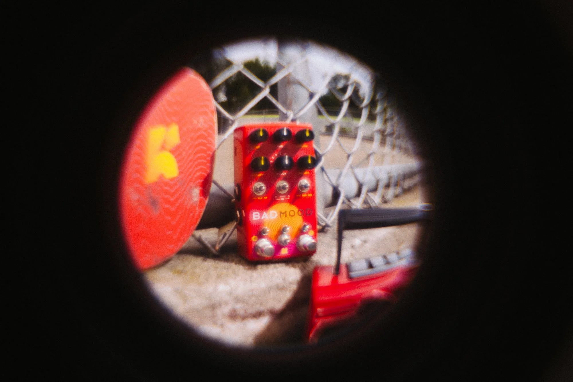 BAD MOOD leaning on a fence next to a skateboard and being seen through a fisheye lense.