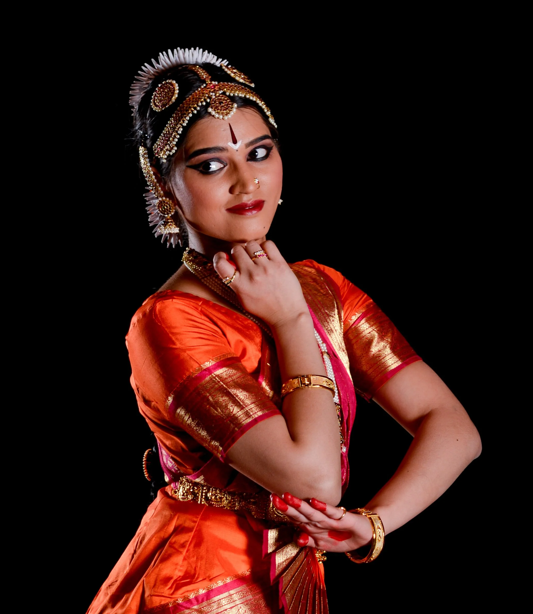 A woman dressed in traditional Indian attire with elaborate jewelry and makeup, posing against a black background.