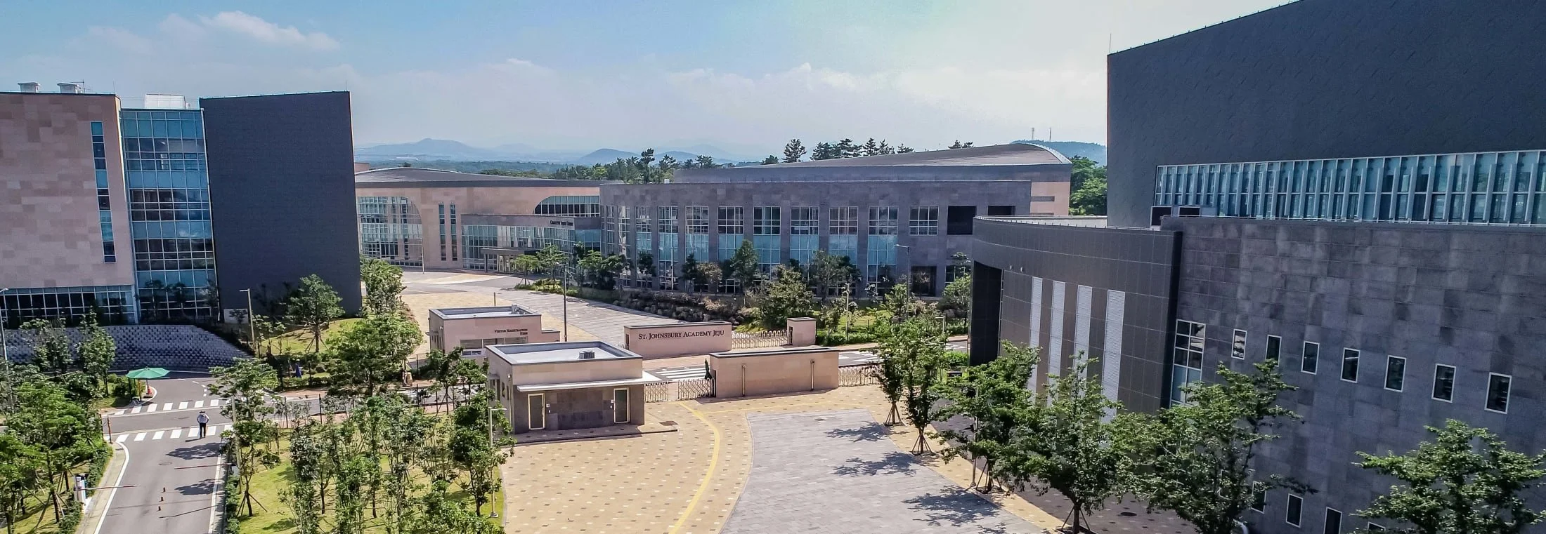 Modern university campus buildings with large glass windows, surrounded by trees, under a partly cloudy sky.
