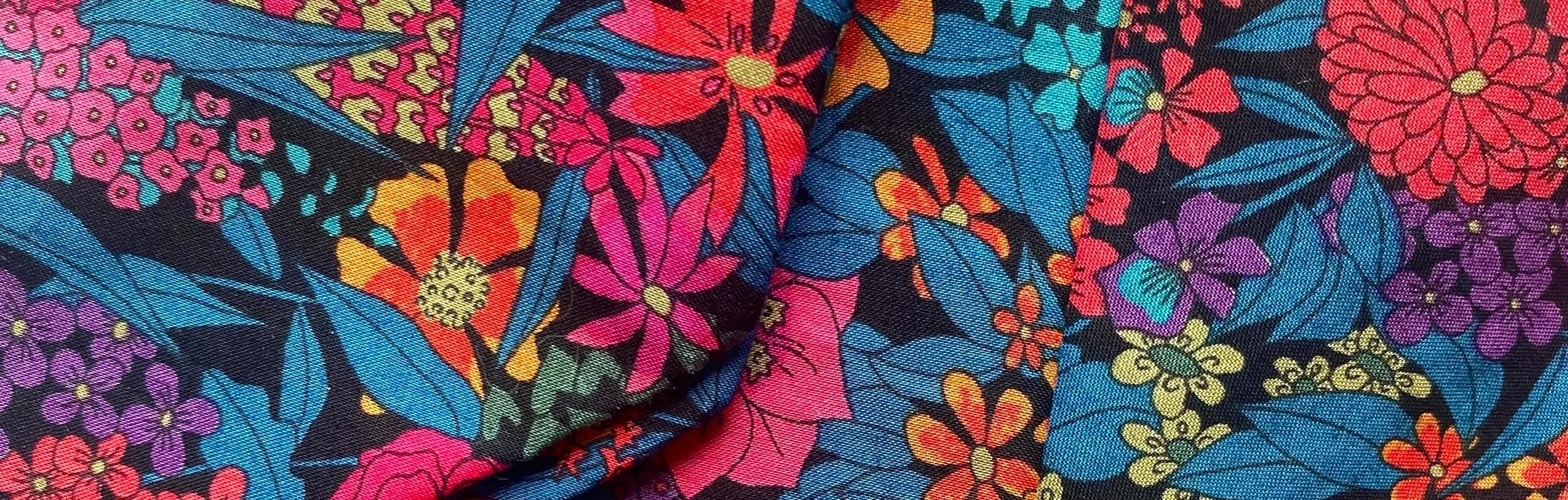Close-up of colourful Liberty London Print floral patterned fabric with pink, purple, yellow, orange, and blue flowers and leaves on a black background. The pattern is called Ciara
