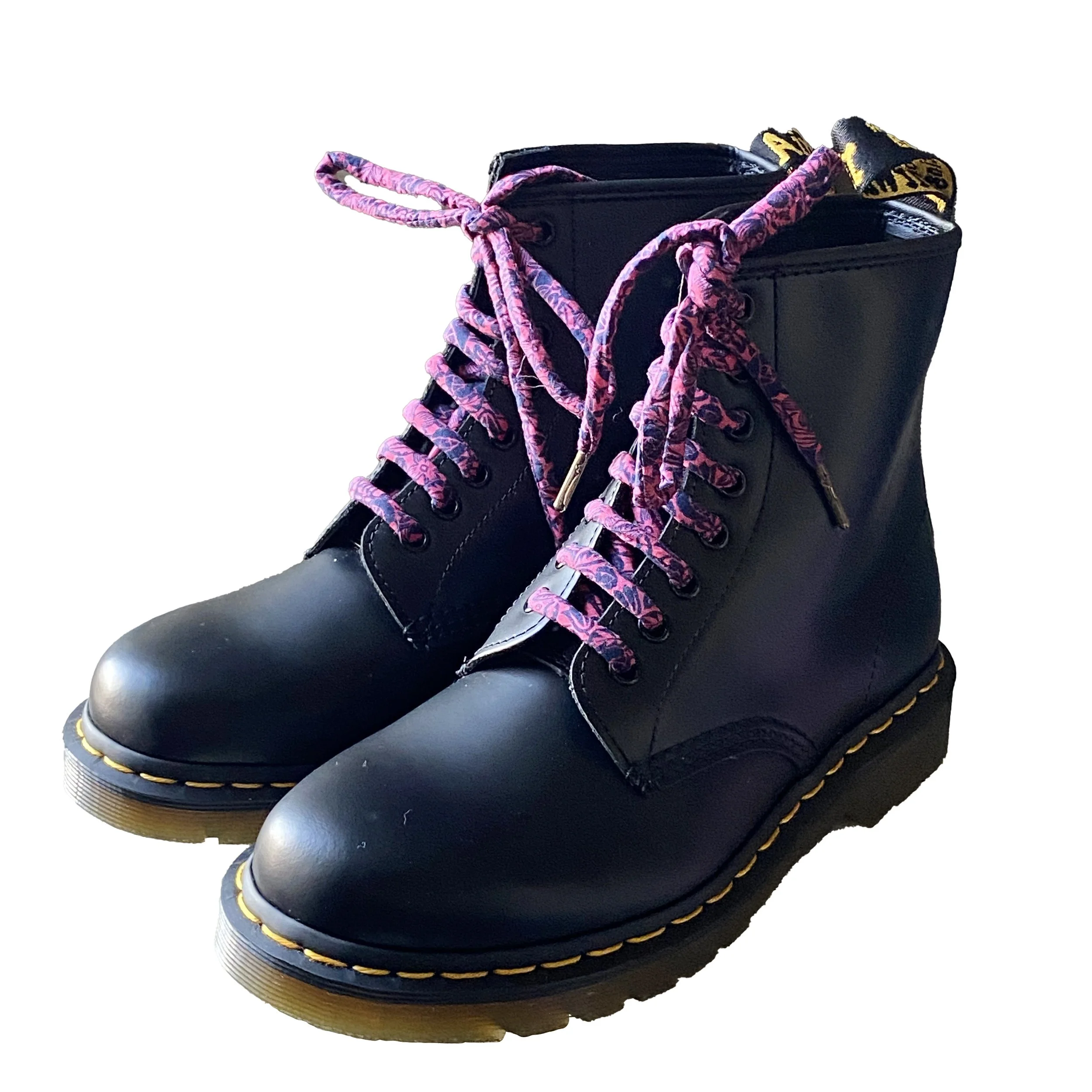 Pair of black leather Dr Marten boots with pink and purple patterned laces and yellow stitching on the sole.