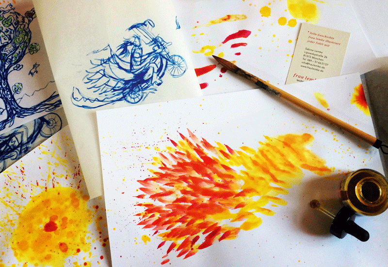 Ein Foto mehrer handgezeichneten Entwürfe, ein paar mit den Farben gelb, orange und rot und ein paar blau. Auf ihnen liegt ein Pinsel.