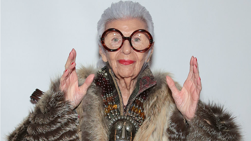 Portrait of an older woman wearing large round glasses and layered jewellery.